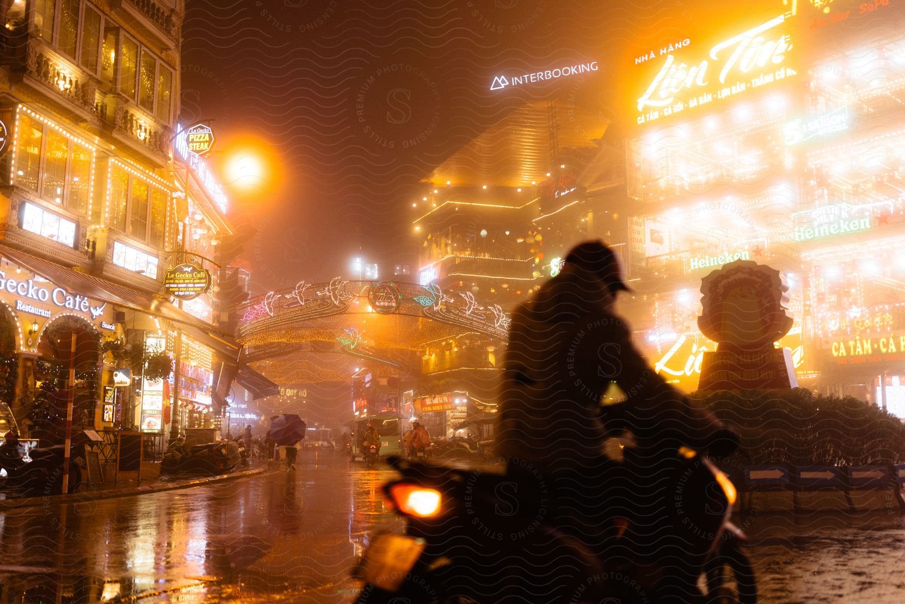 Asian city at night with a person riding a motorcycle and other vehicles in the background