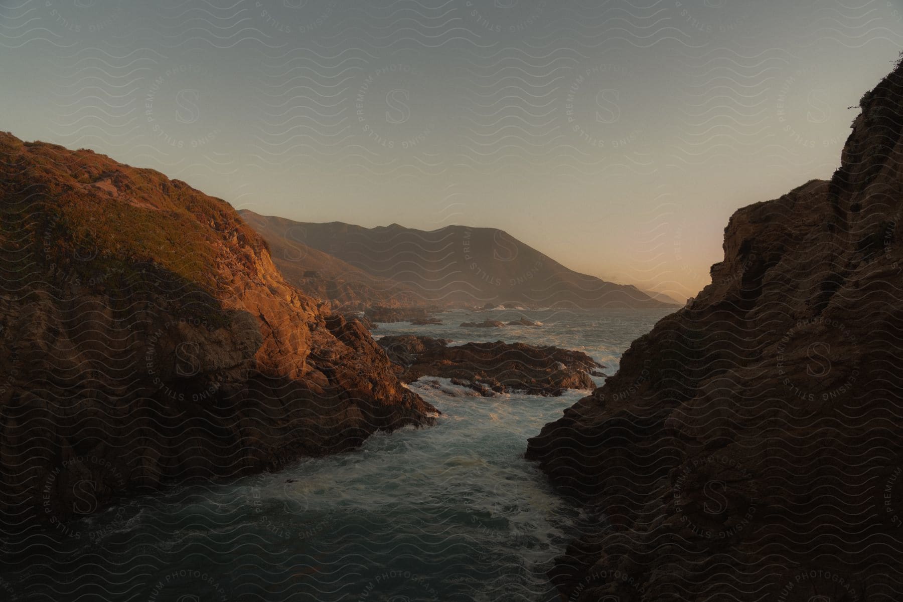 River water splashes against rocks in a mountainous landscape under a hazy sky