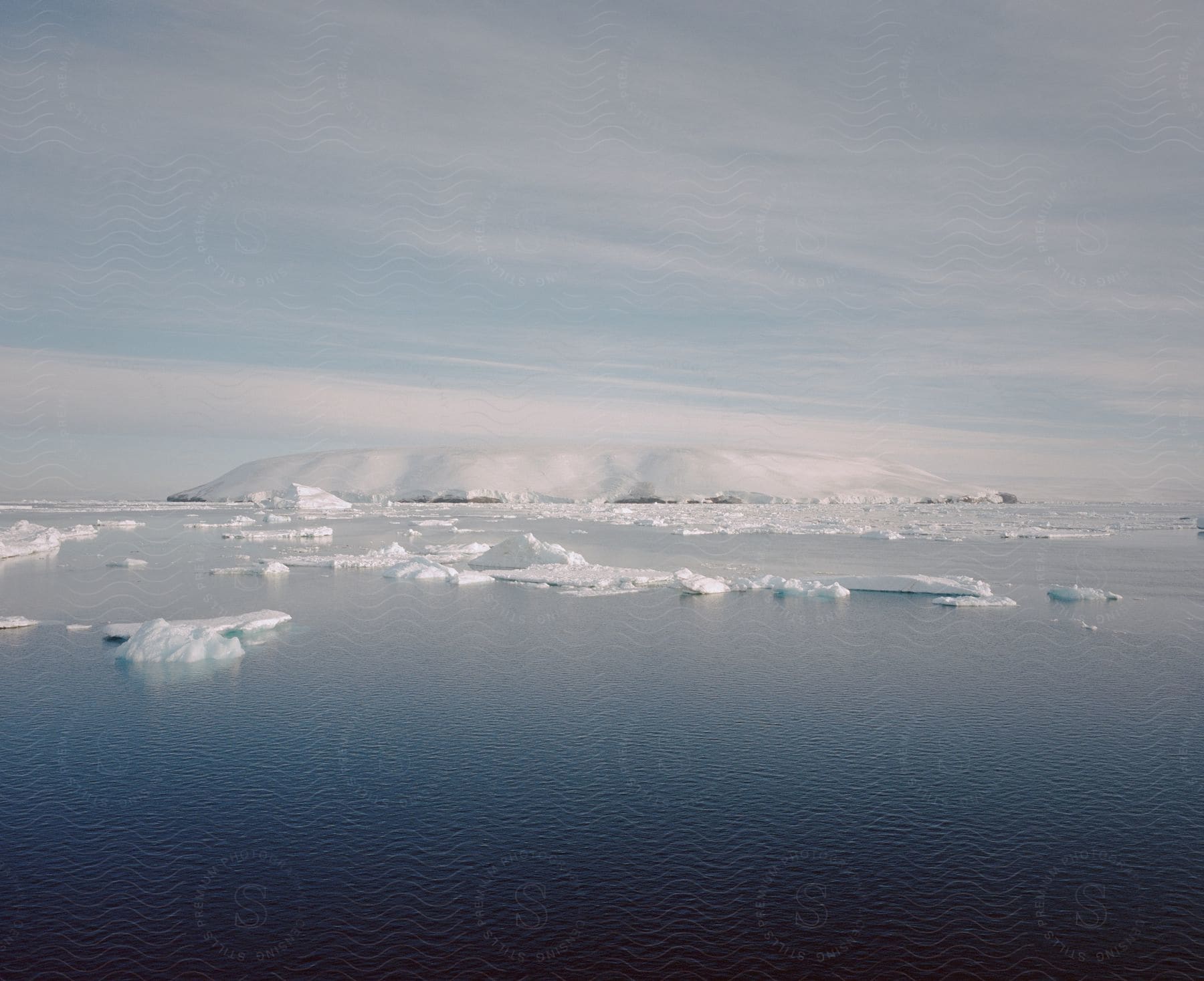 Ice caps and an iceberg float on serene water in a landscape