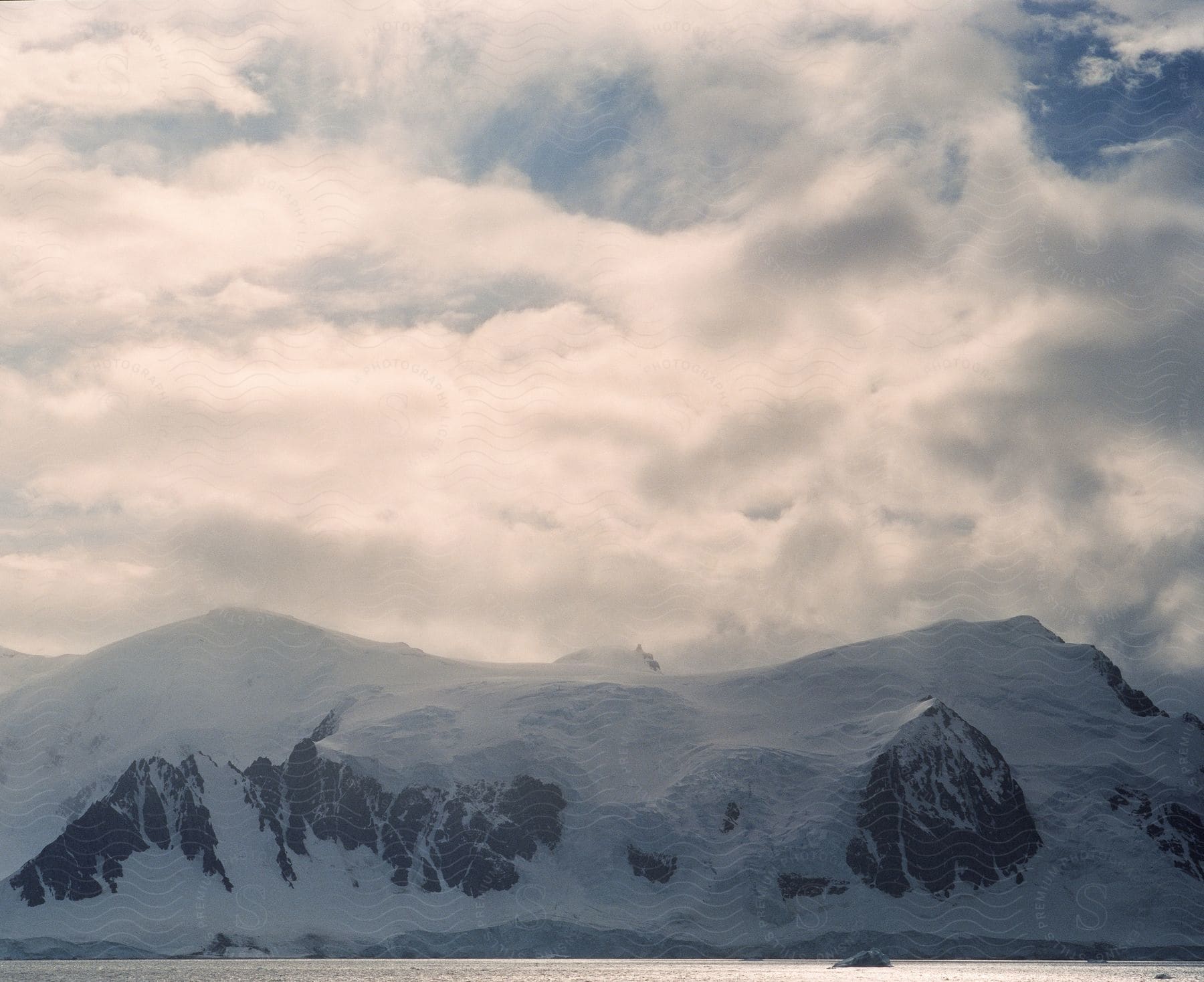 Snowy coastline and mountains against cloudy sky in a winter landscape