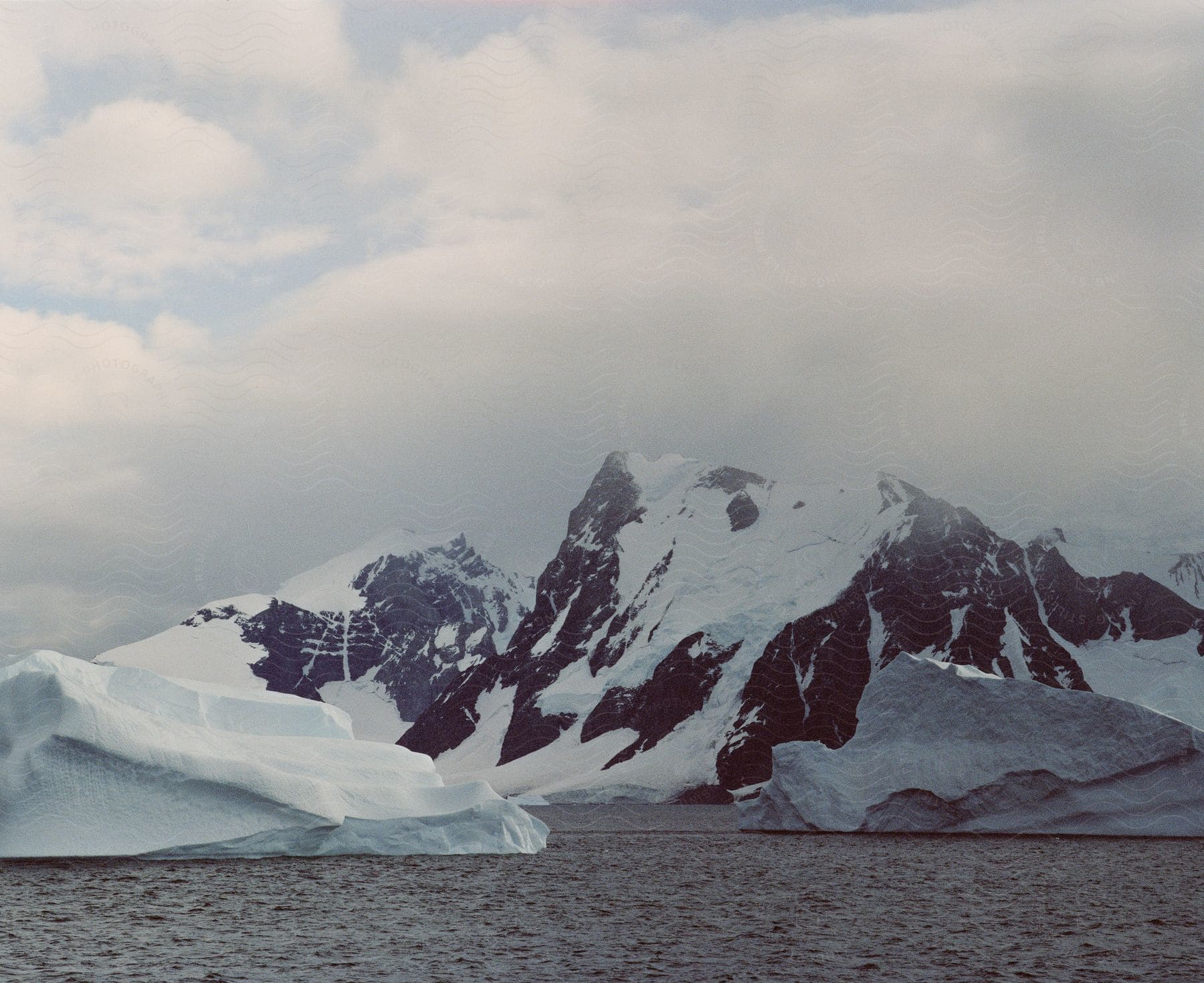 Closeup of icebergs amidst glacierdraped mountains under cloudy skies