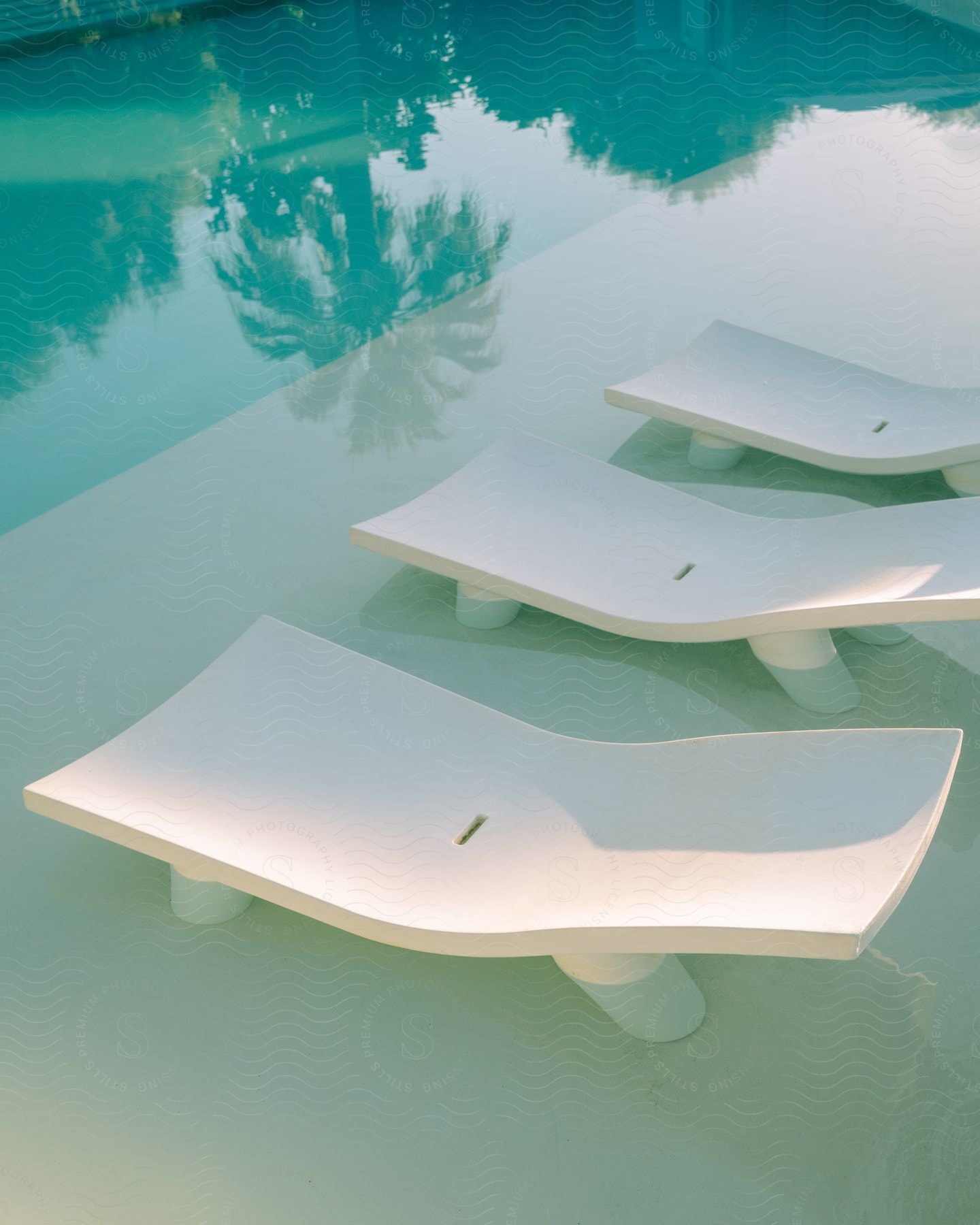 Poolside with modern white chaise lounge chairs and a reflection of a palm tree on the pool during daytime