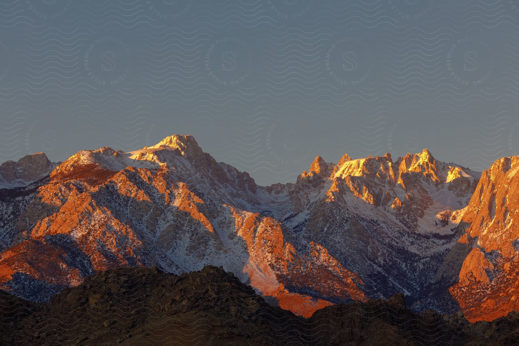 Snowcovered mountain range with colorful sunset or sunrise and soil in the foreground on a cloudless winter day