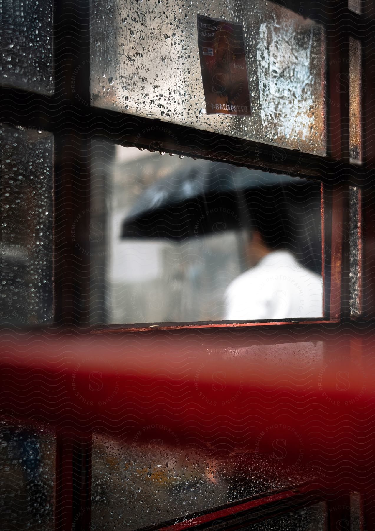 A man holding an umbrella seen through a raincovered window