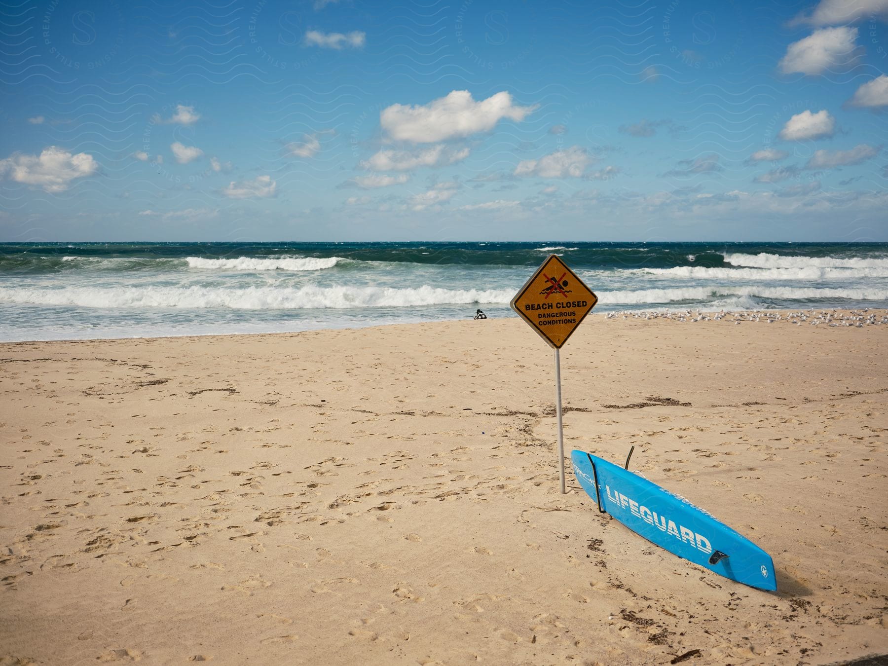 Yellowcolored sand beach with beach closed sign and lifeguard surfboard