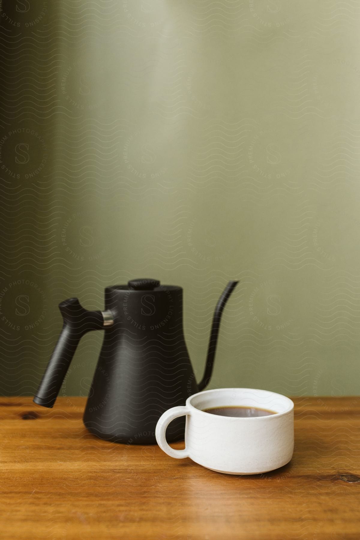 A modern black teapot and white tea cup on a wood table in front of a grey wall