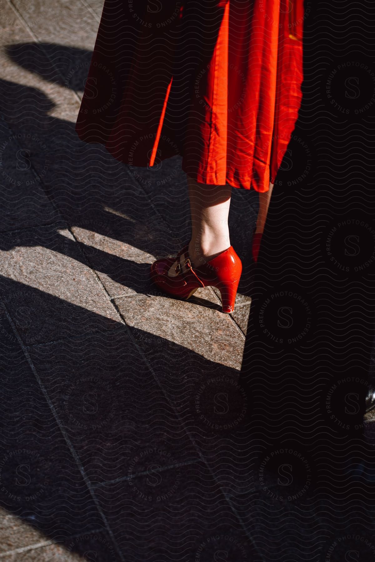 A woman in a red dress and high heels walking on a road surface