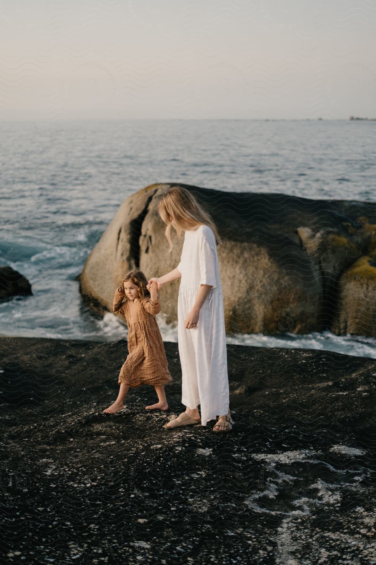 Mother and daughter walk along holding hands on a beach with large rocks