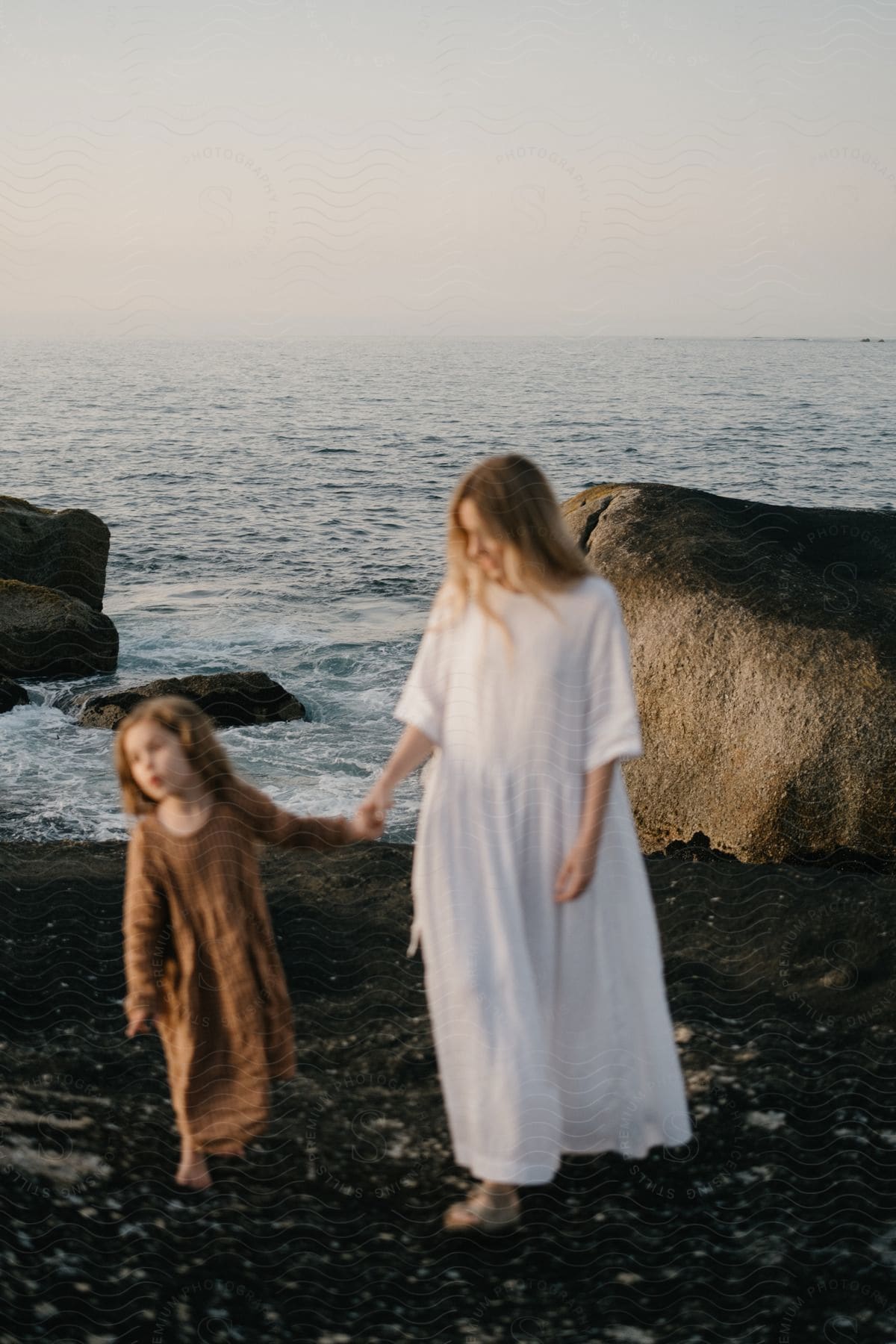 A mother and daughter walk along a black sand beach