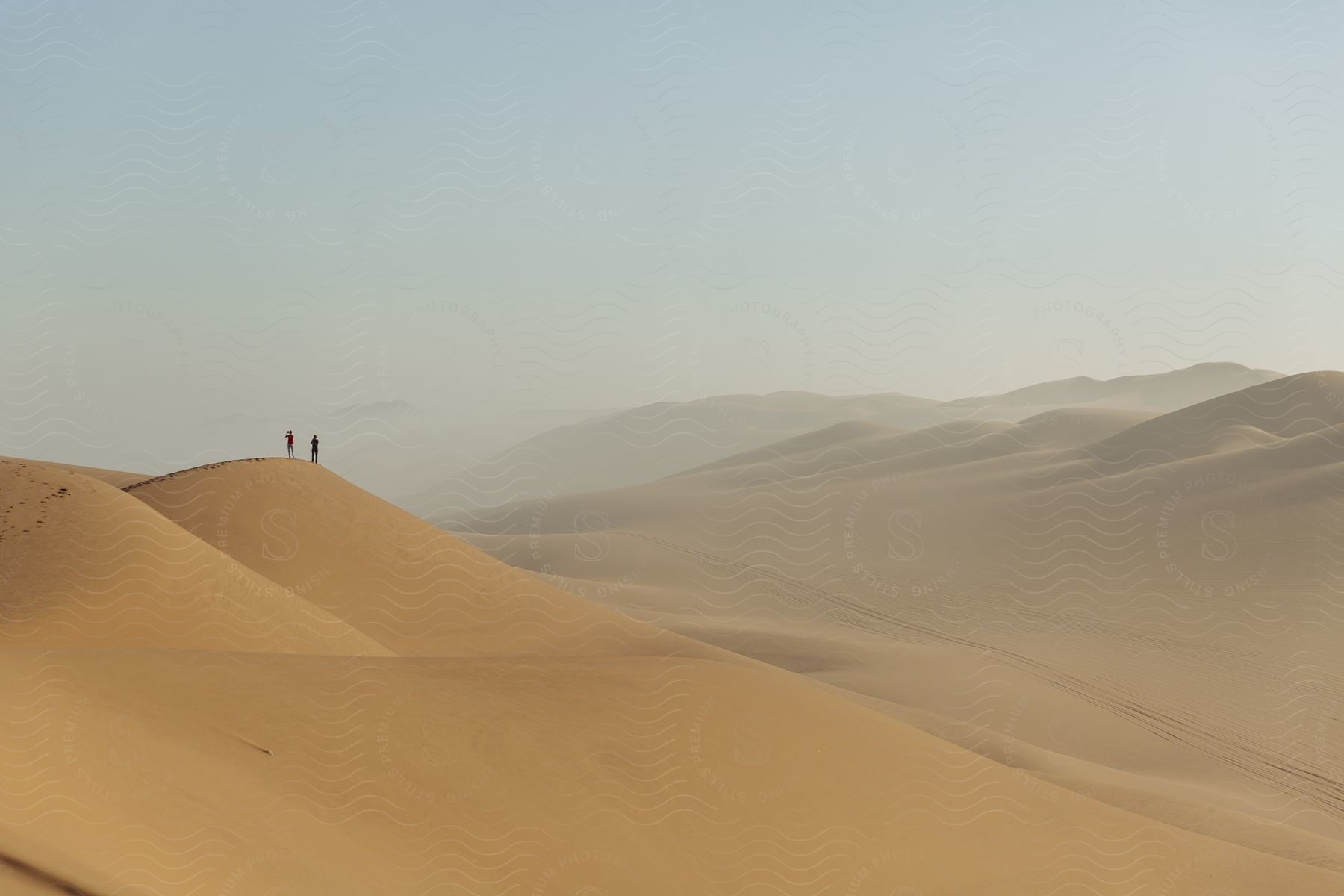 Two people standing on the peak of a sand dune in a desert