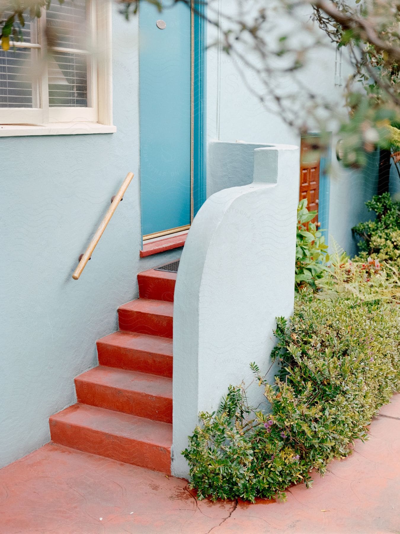Red brick stairs leading to a light blue door of a house with the house and the wall covering the stairs also light blue
