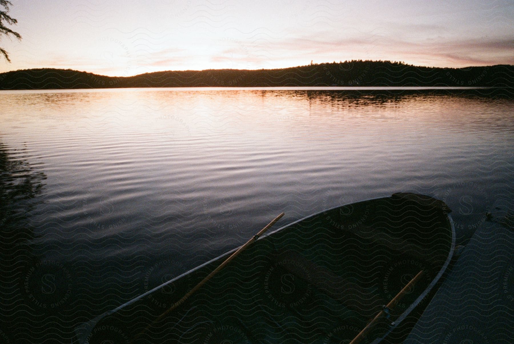 A small paddle boat on the bank and the silhouette of the hills on the opposite side at sundown