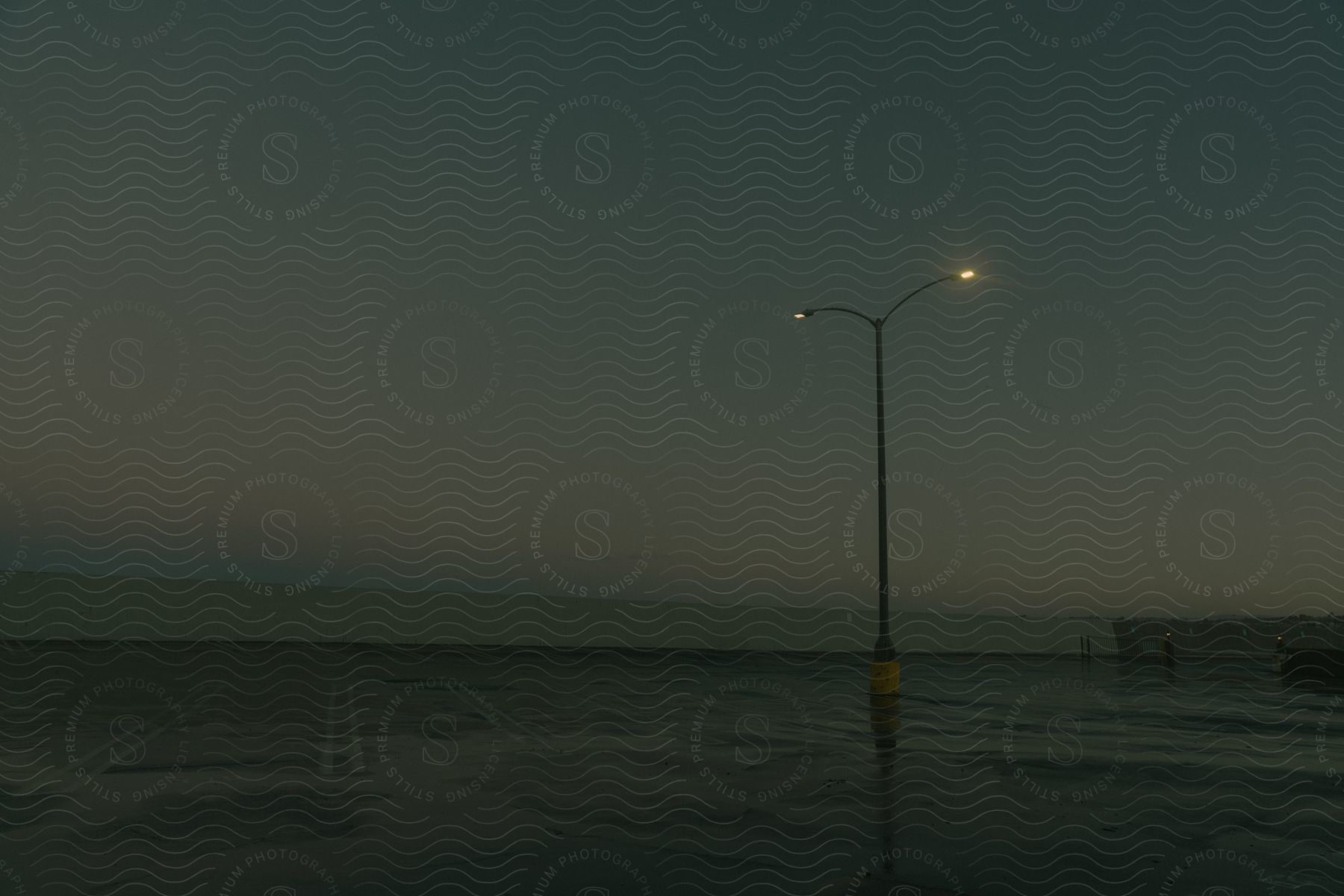 Street lights illuminate a damp parking lot along the coastline under a dark gray sky