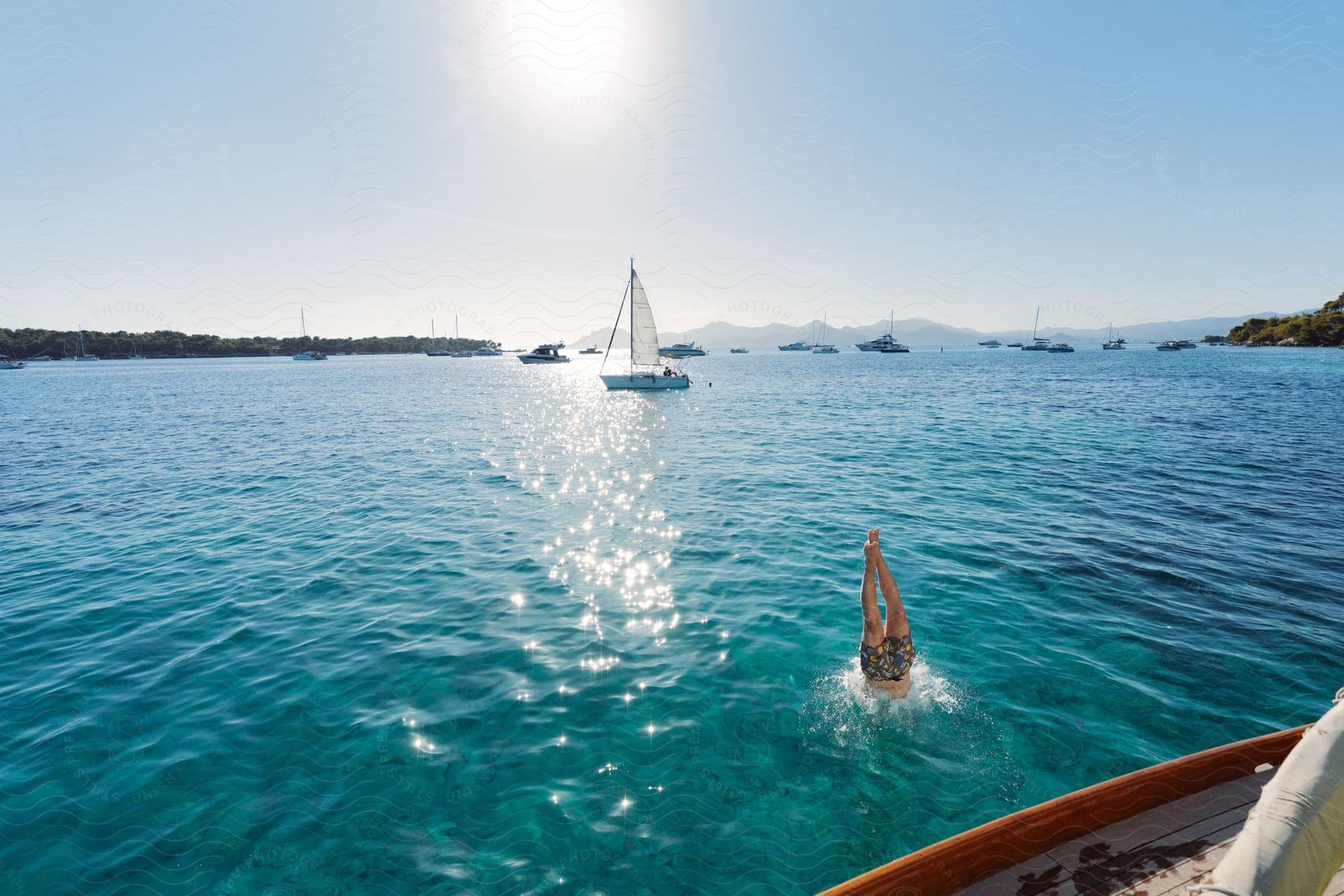 Afternoon sun reflecting off blue ocean water a sailboat with a white sail and a man diving into the water off a boat in the french riviera