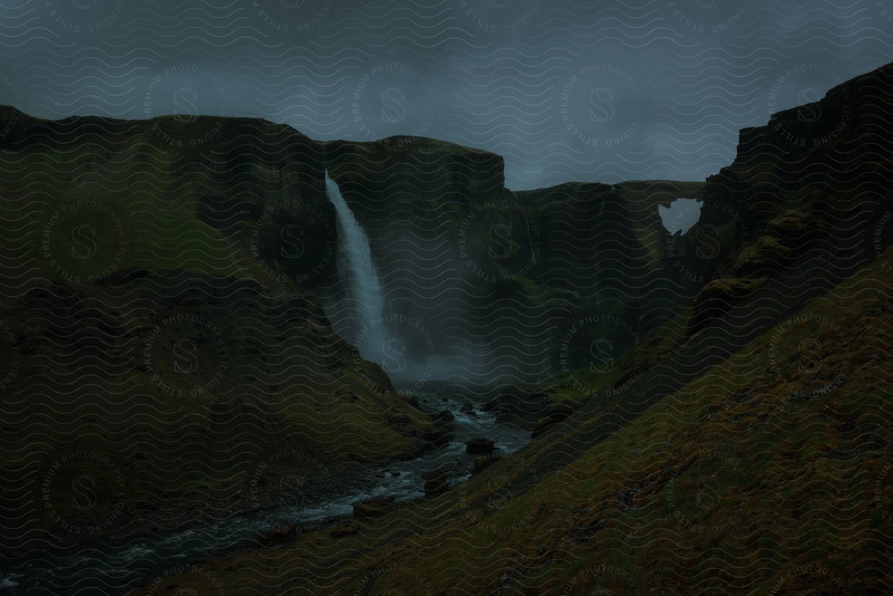 Waterfall feeding into a water stream between hills in a dark and cold natural landscape