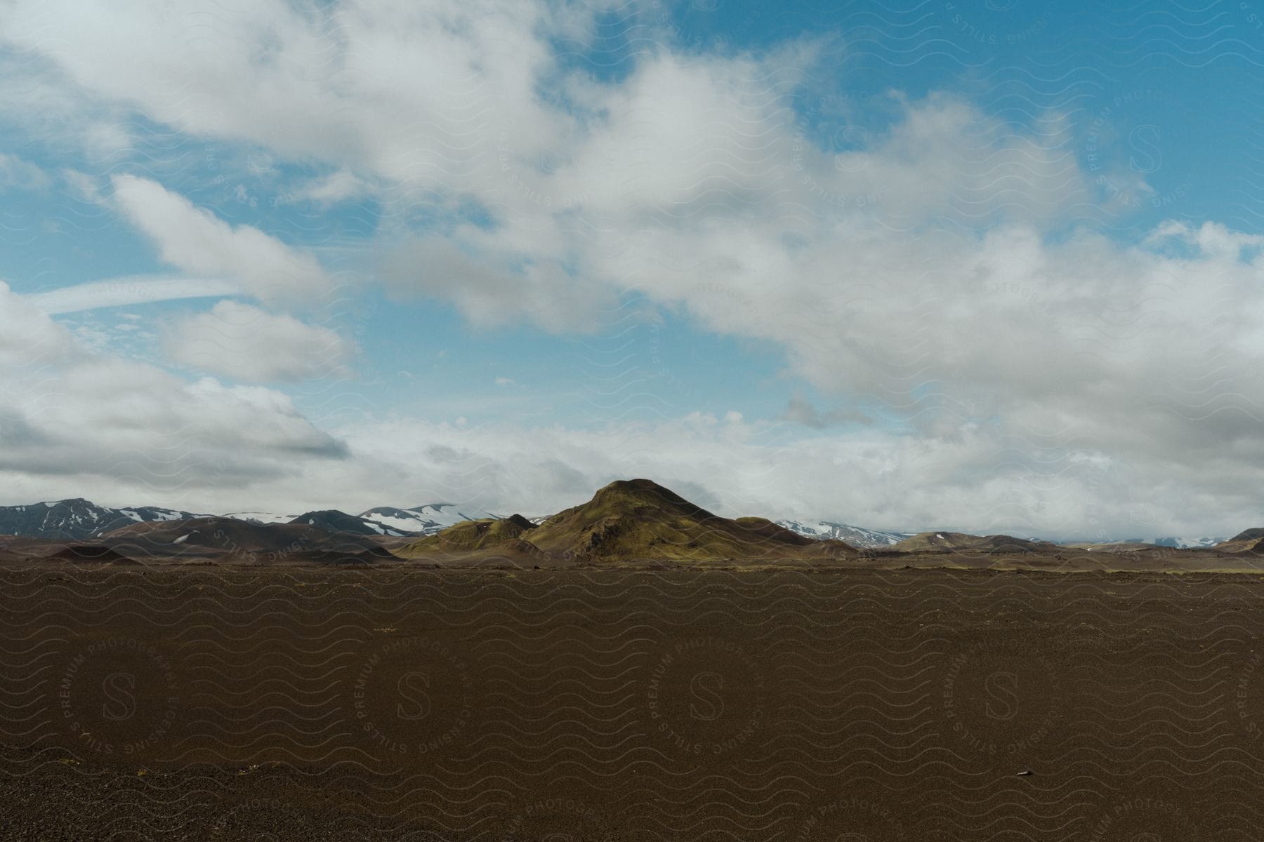 Flatlands under cloudy sky with snowcovered mountains in the background