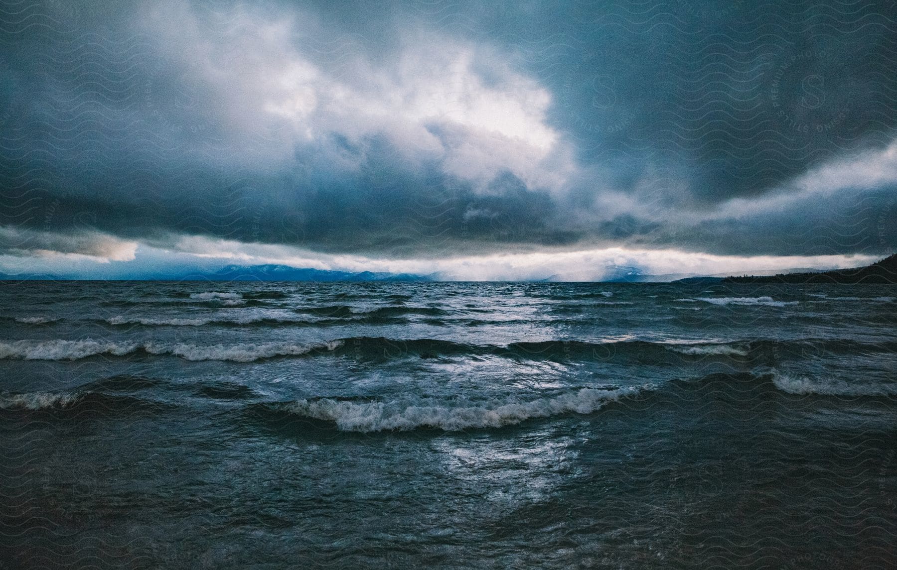 Rough water waves roll into shore as dark clouds hang overhead at an exterior location during the day