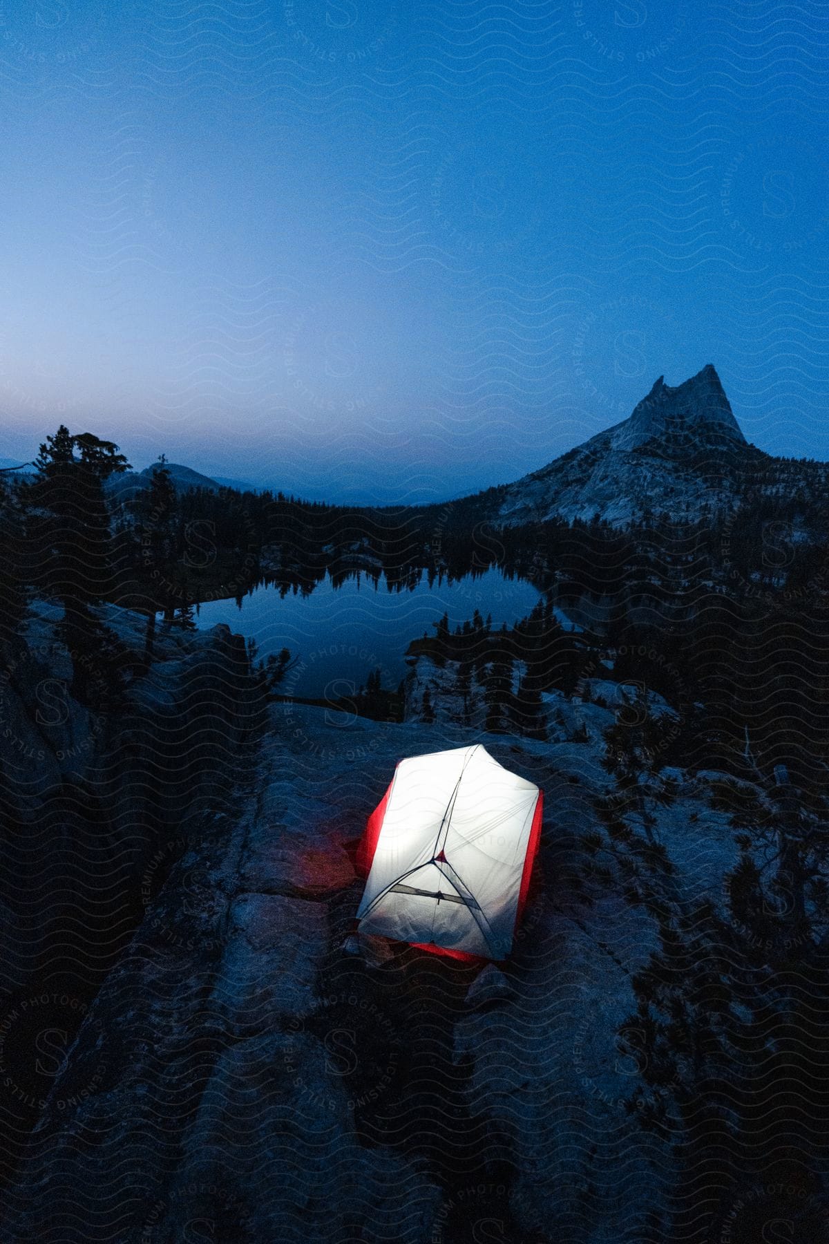 A tent is illuminated at night overlooking a small lake in a mountain valley