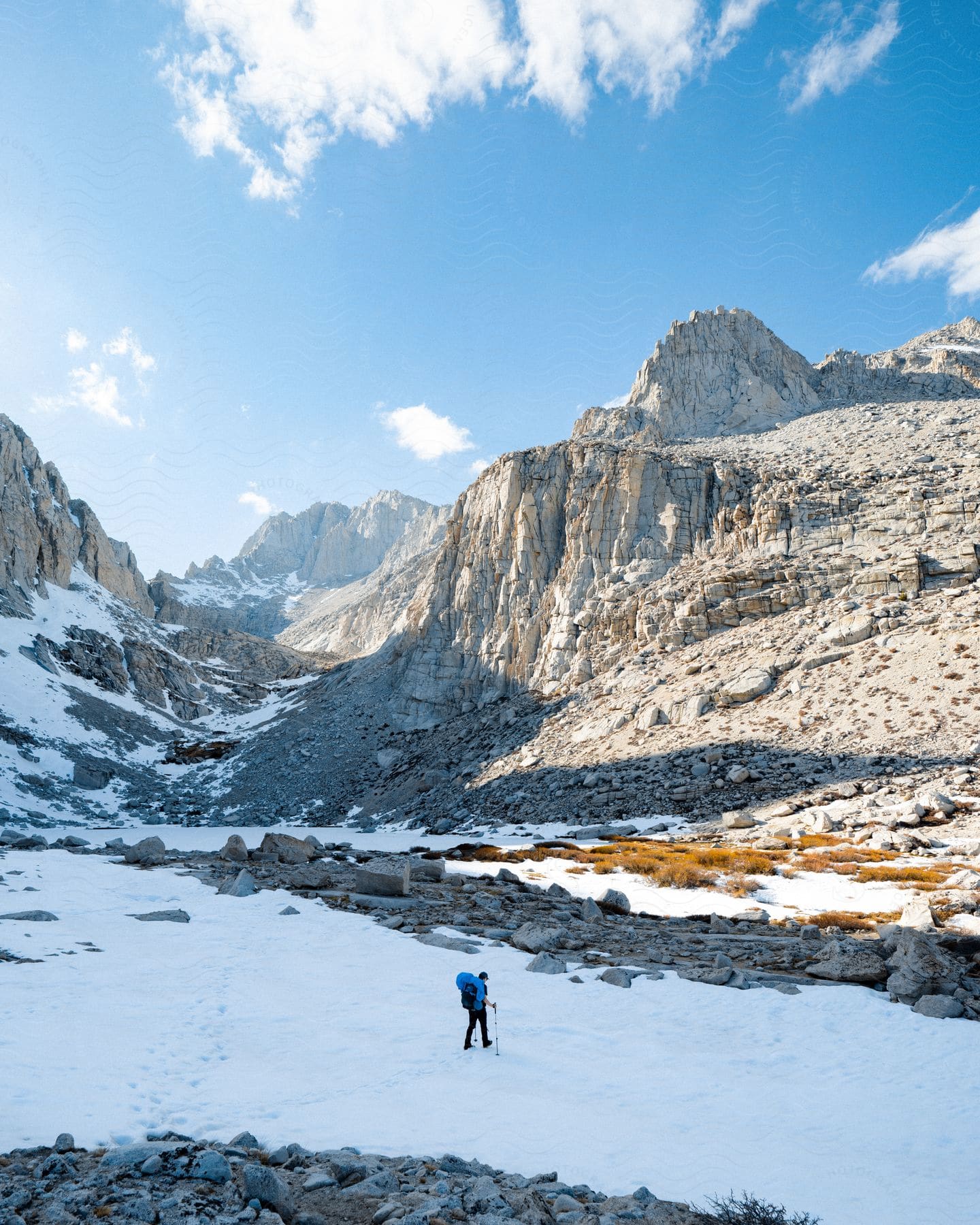 Hiker walking through snowcovered mountain valley with backpack and trekking poles under sunny mountains