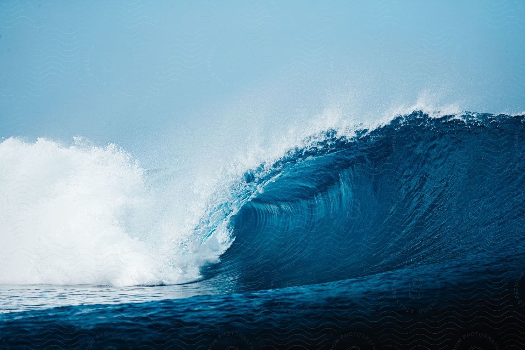 A giant wave in the ocean under a light blue sky with a large light white cloud in the day