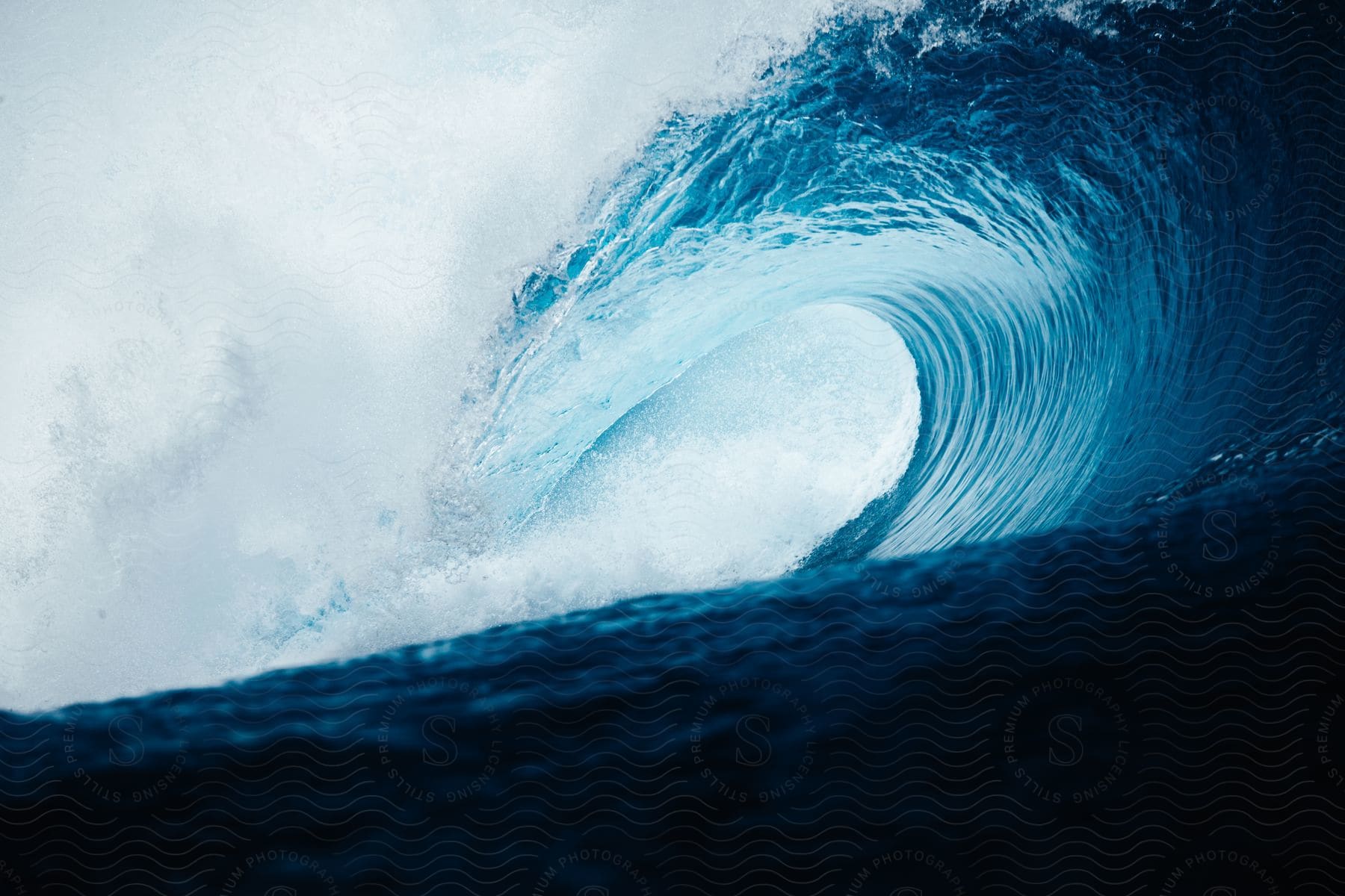 A Blue Wave Crashes Onto The Shore Under A Cloudy Sky