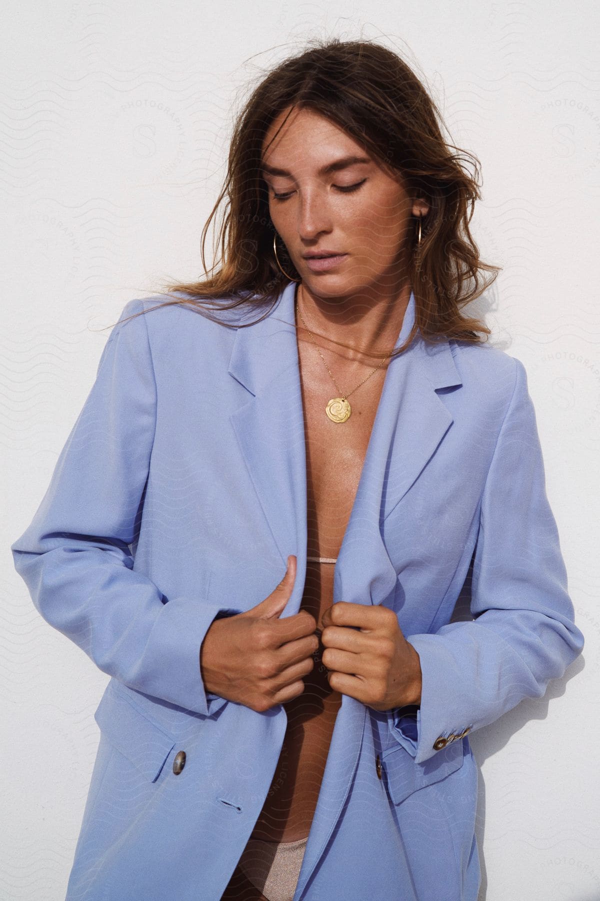 Woman posing wearing blue blazer over white bikini looking down on the beach