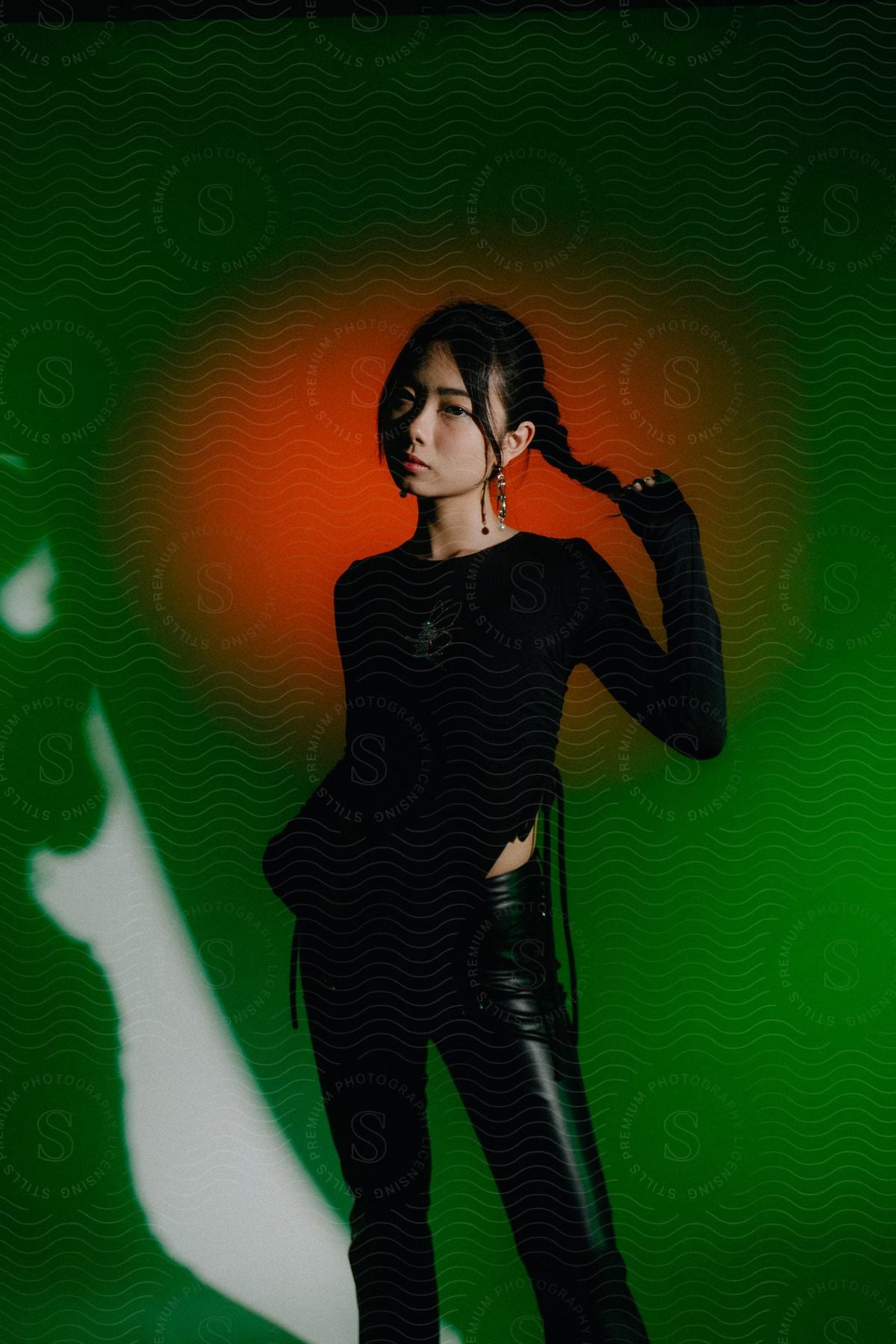 A female model wearing black clothing and holding her hair with one hand in a studio shoot