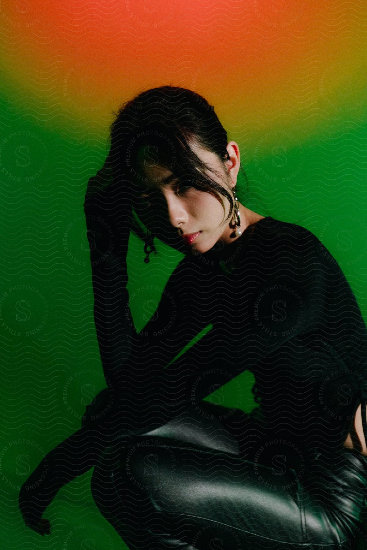 Woman in black shirt and leather pants poses on green and red background