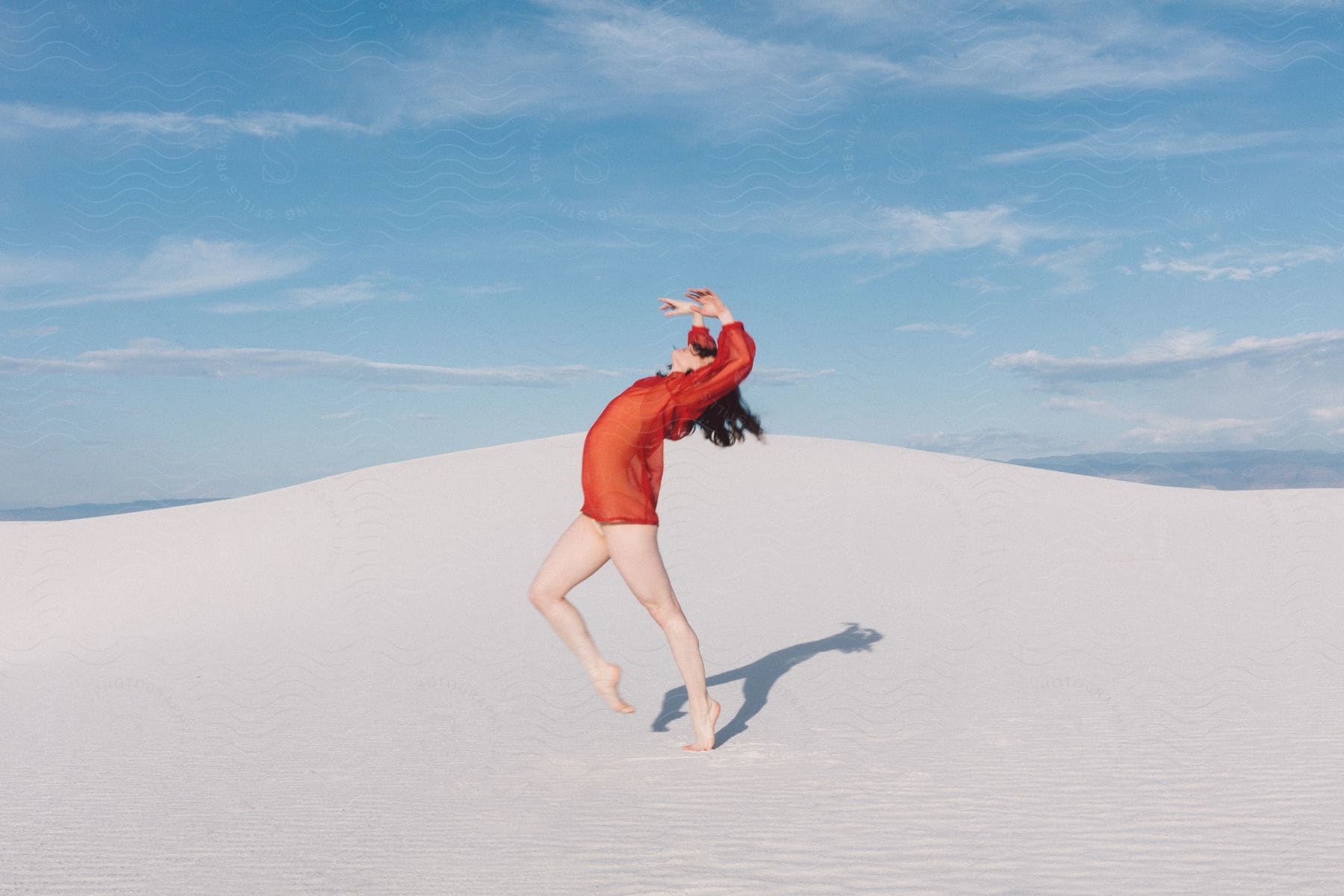 A woman wearing a red shirt dances in the desert during the day