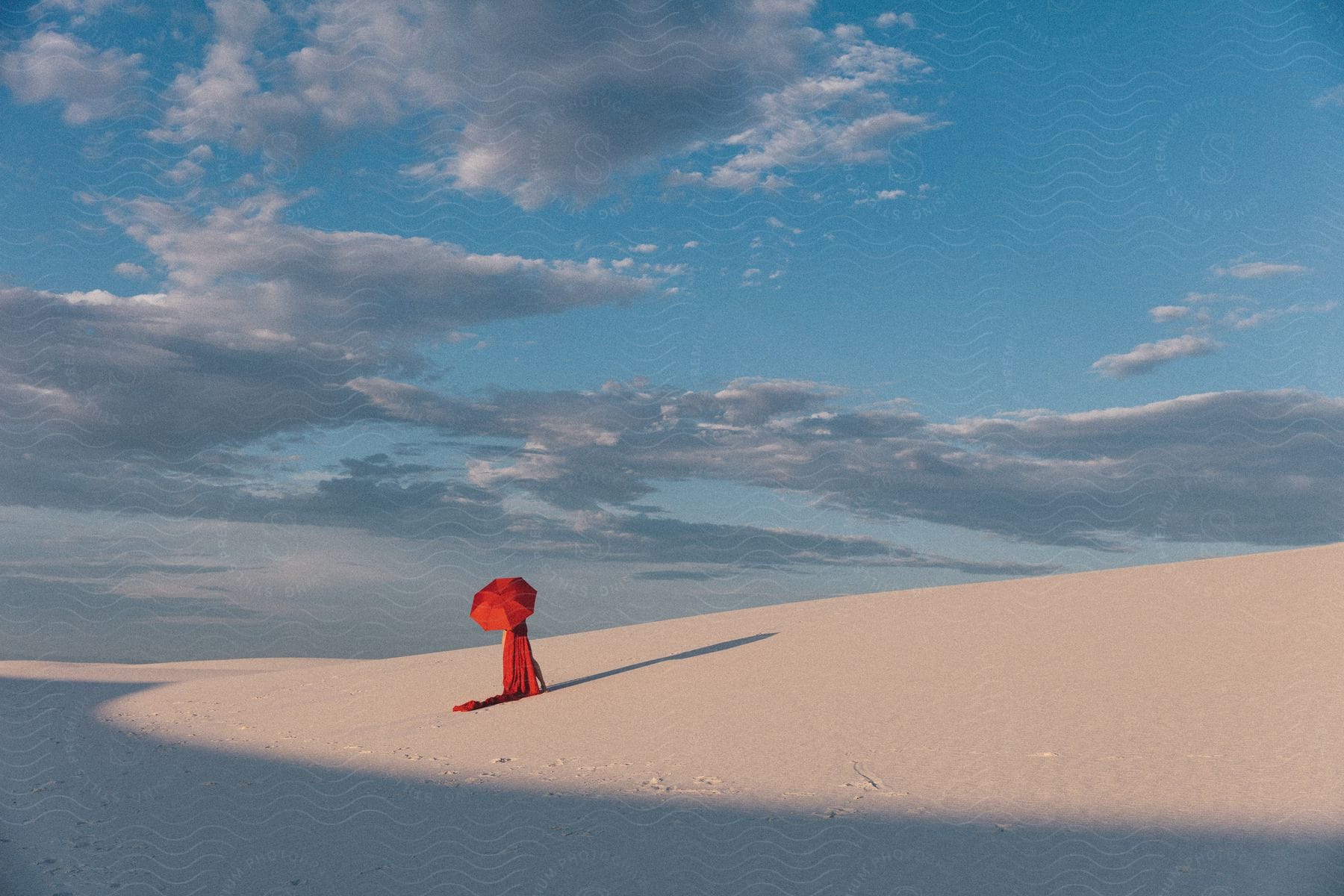 A woman in a red dress holds an umbrella as she stands in a desert looking away