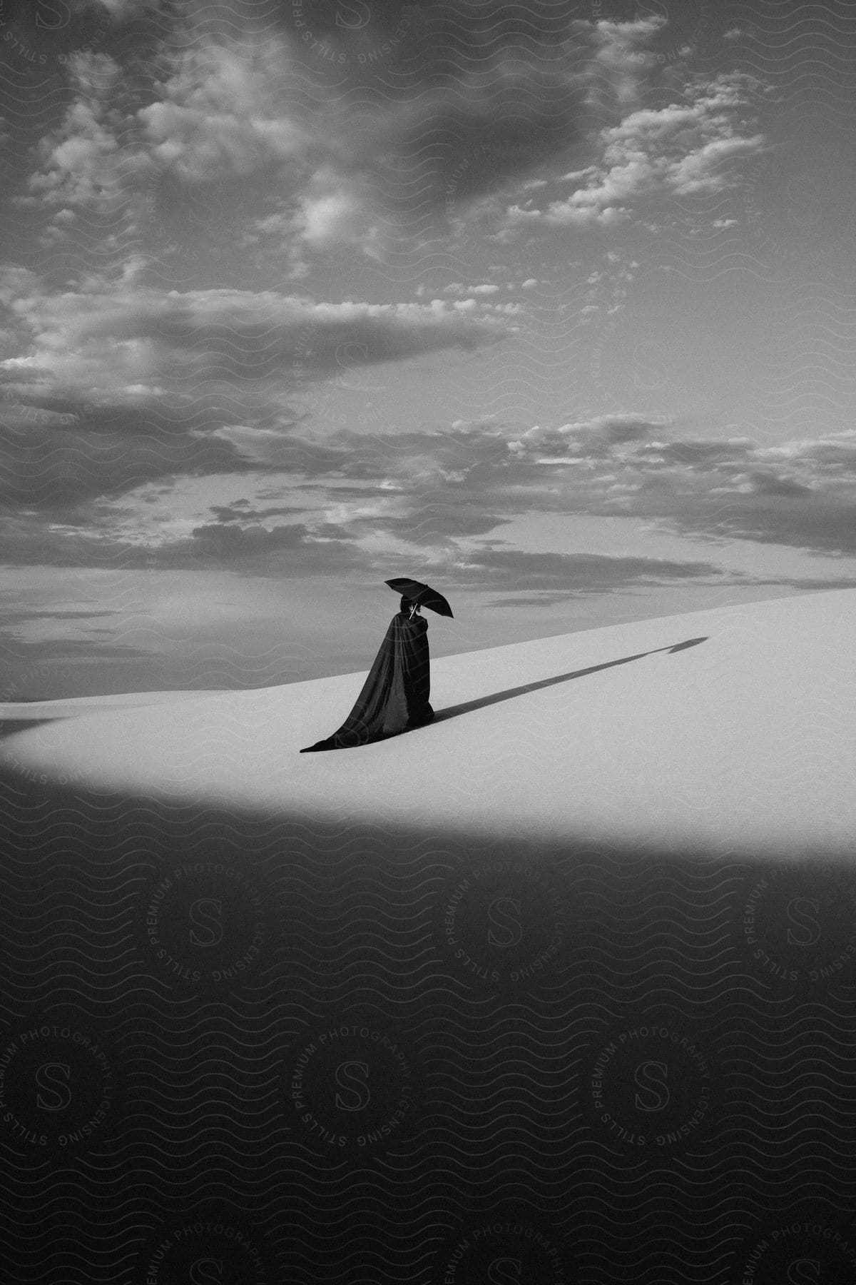 Woman in a black cloak holding an umbrella casting a shadow on the sand in the outdoors