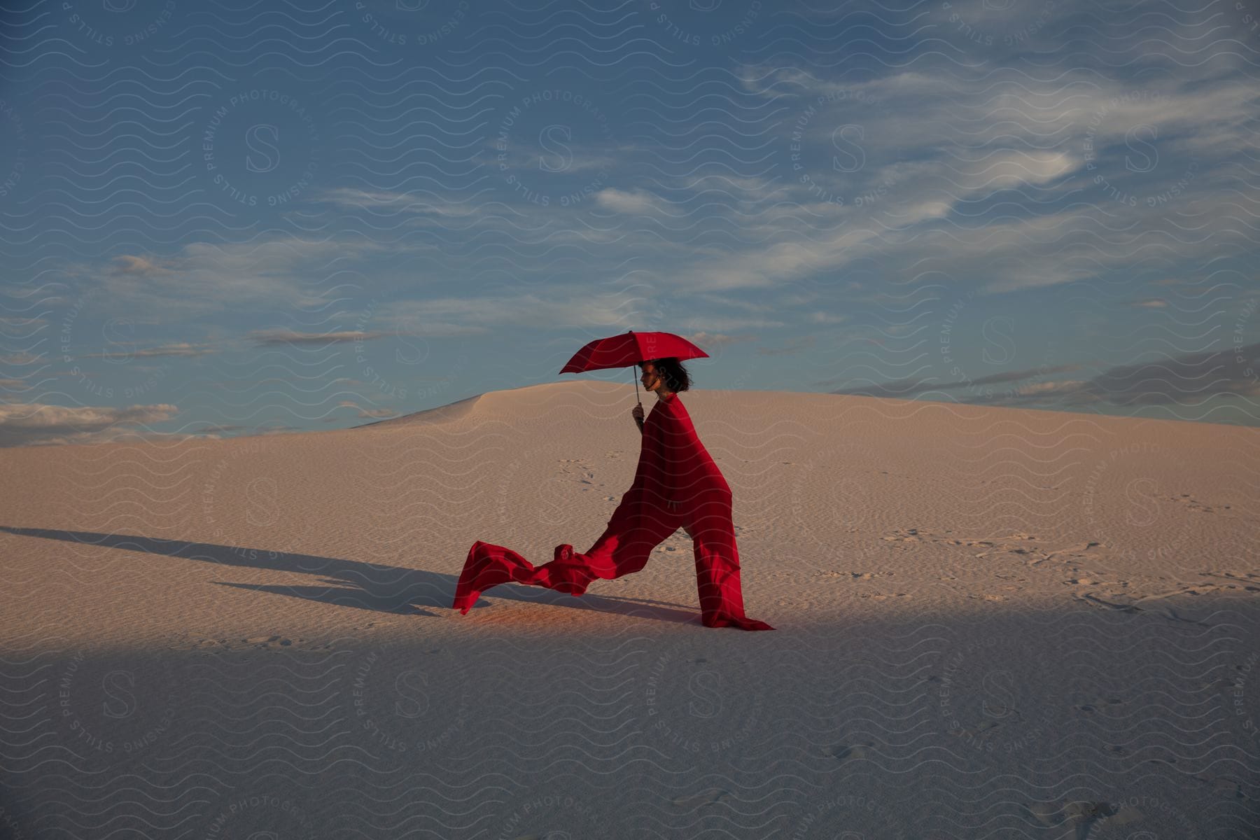 A Woman Wearing A Red Robe And Carrying A Red Umbrella Stands In The Desert