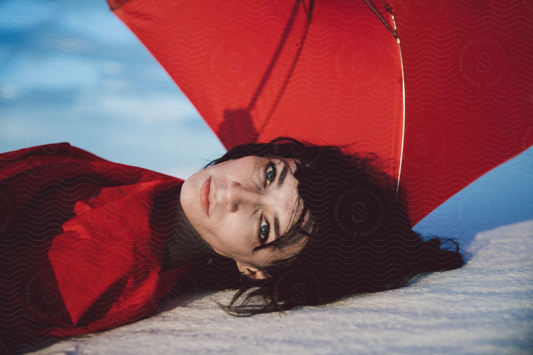 Woman Lying On Ground Gazing Into Camera With Red Umbrella Behind Her