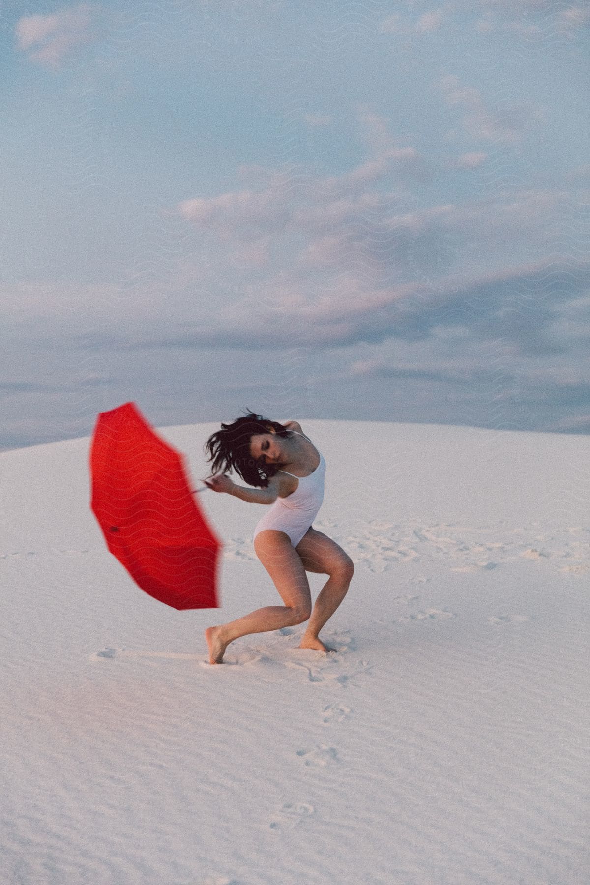 Woman in white bathing suit holds red umbrella in contorted dance position