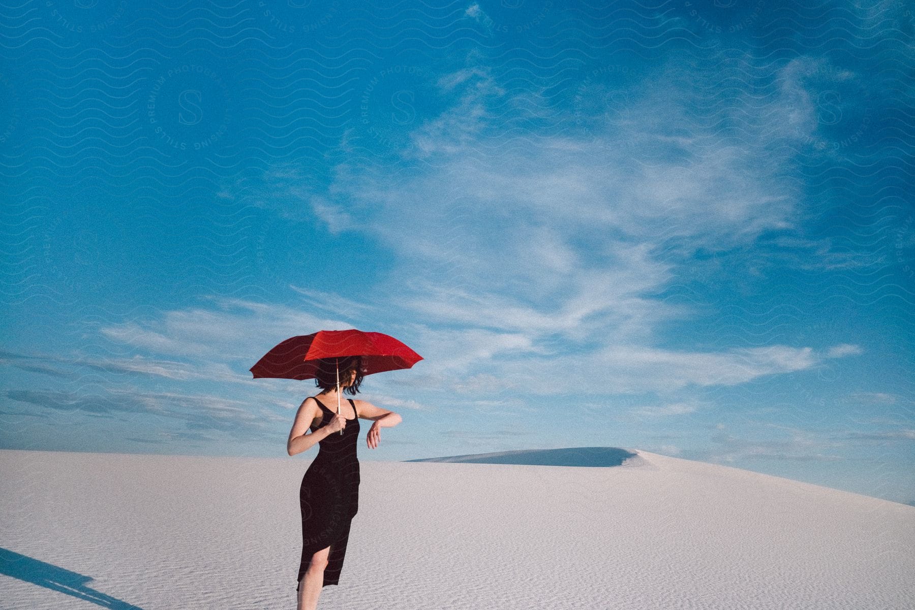 Woman in black dress with red umbrella in desert under blue sky