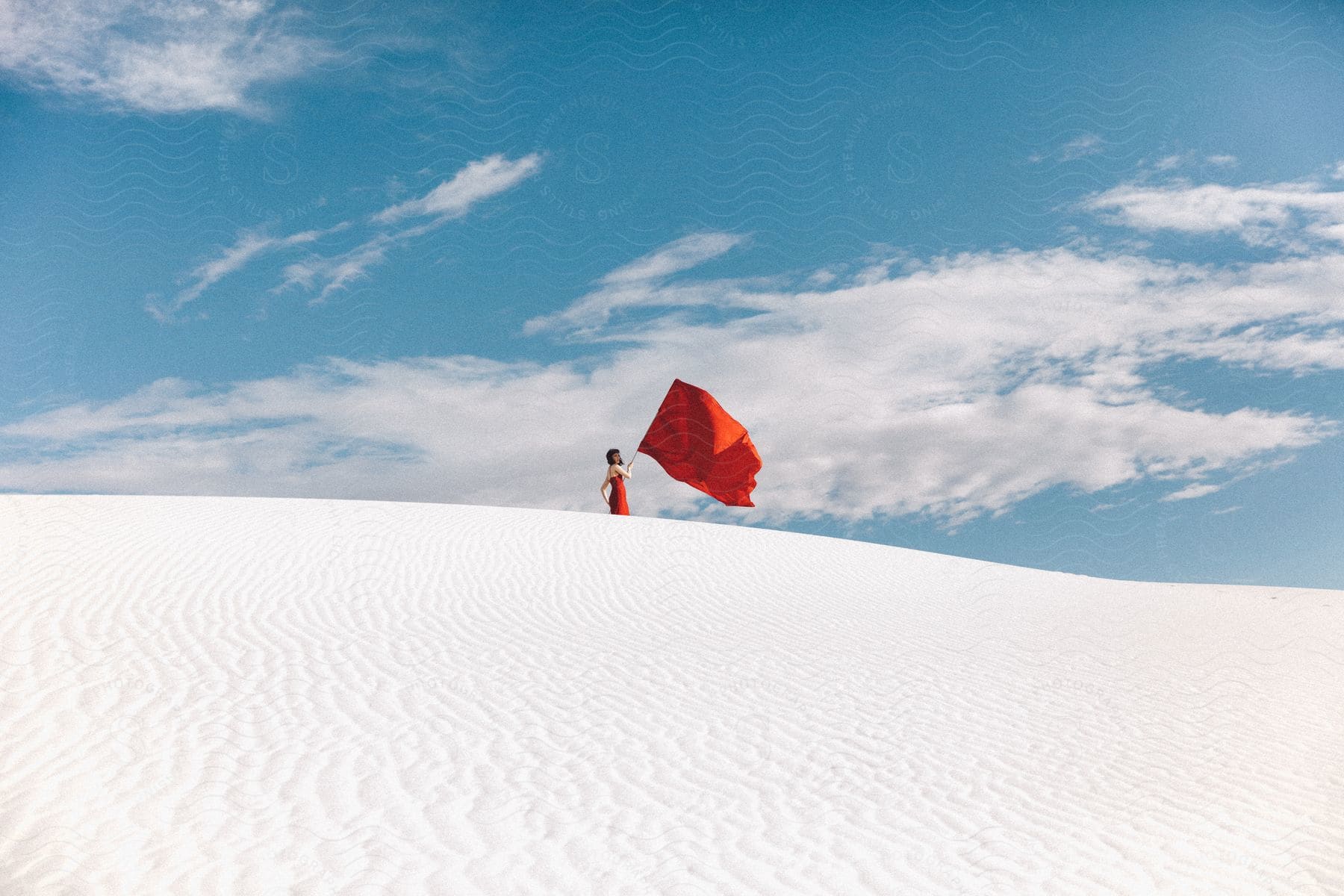 A woman holds a red flag in the desert wind