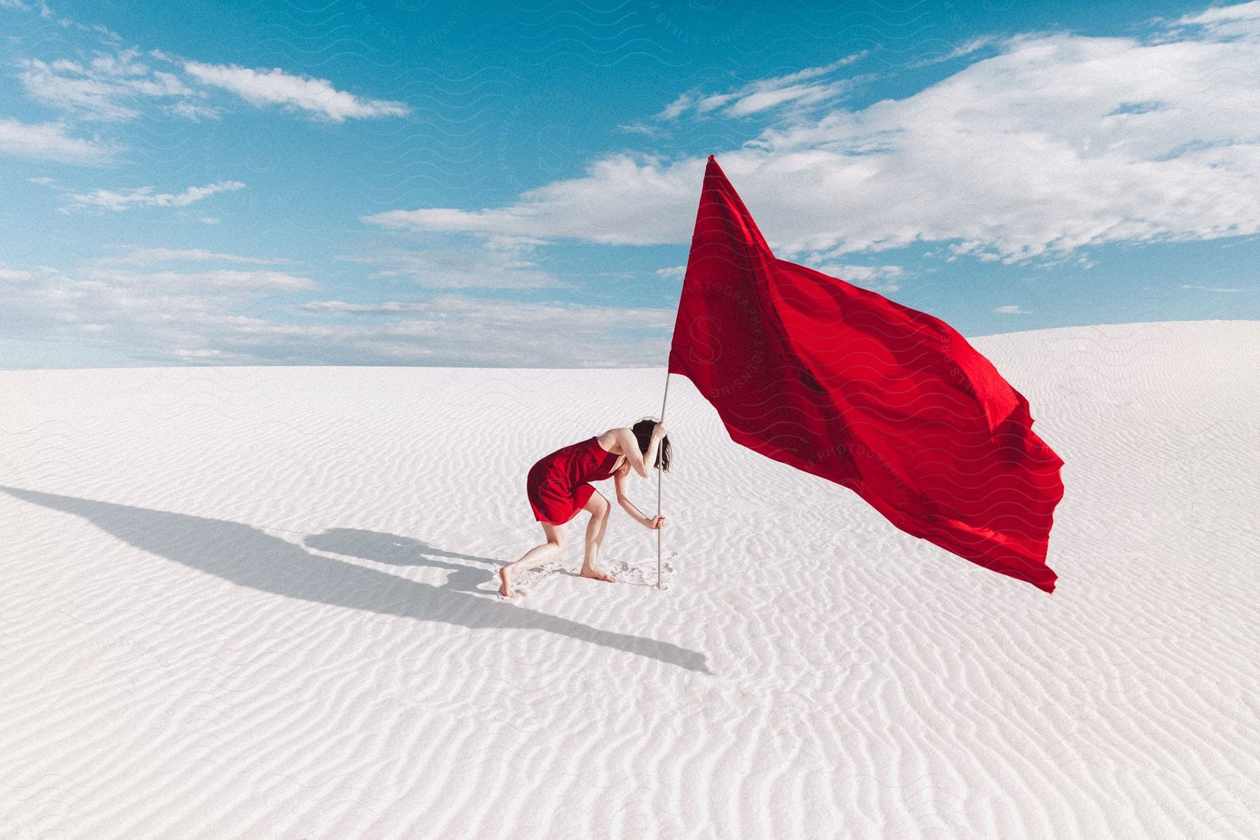 A woman in a red dress planting a flag in the sandy desert under the bright sun