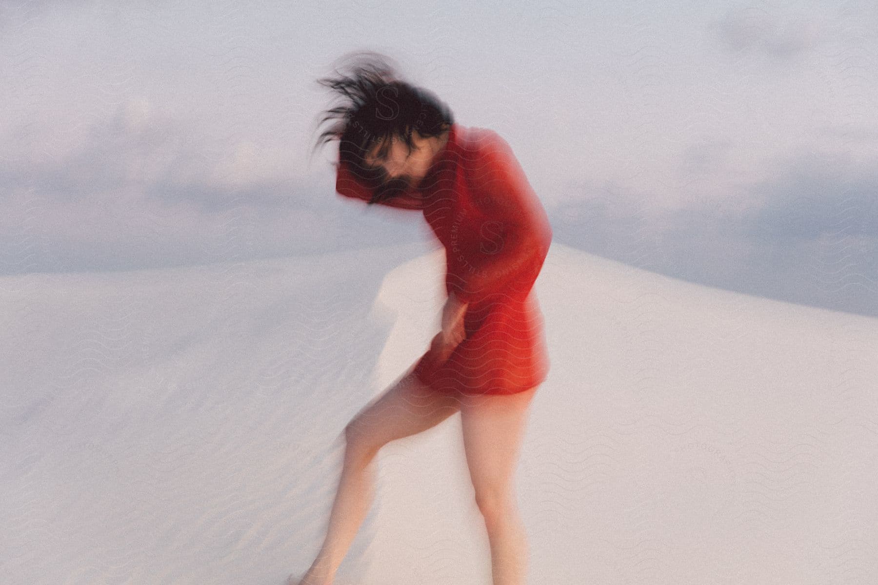 A Woman In A Red Dress Walks On A Sand Dune Scratching Her Head