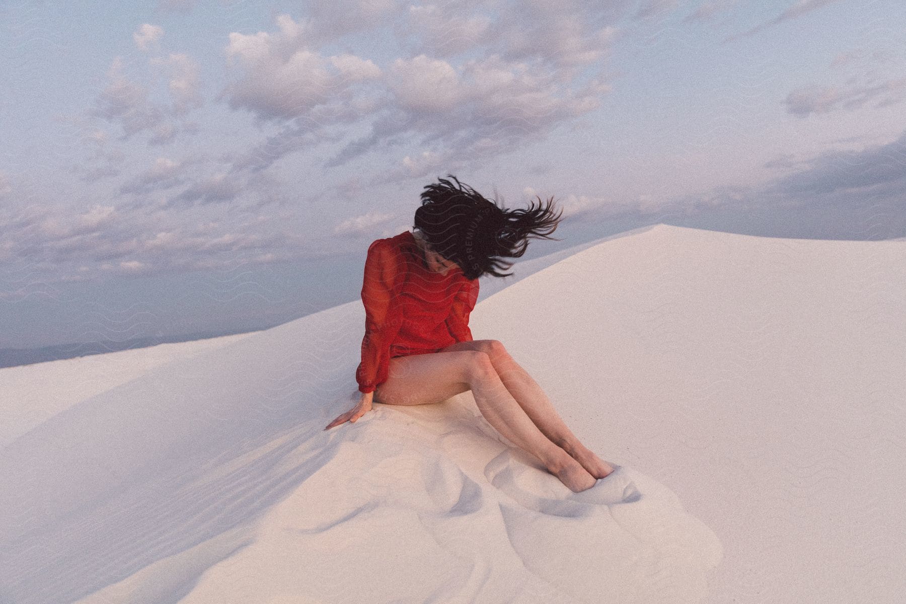 Woman in red sitting in sand with hair blowing in wind