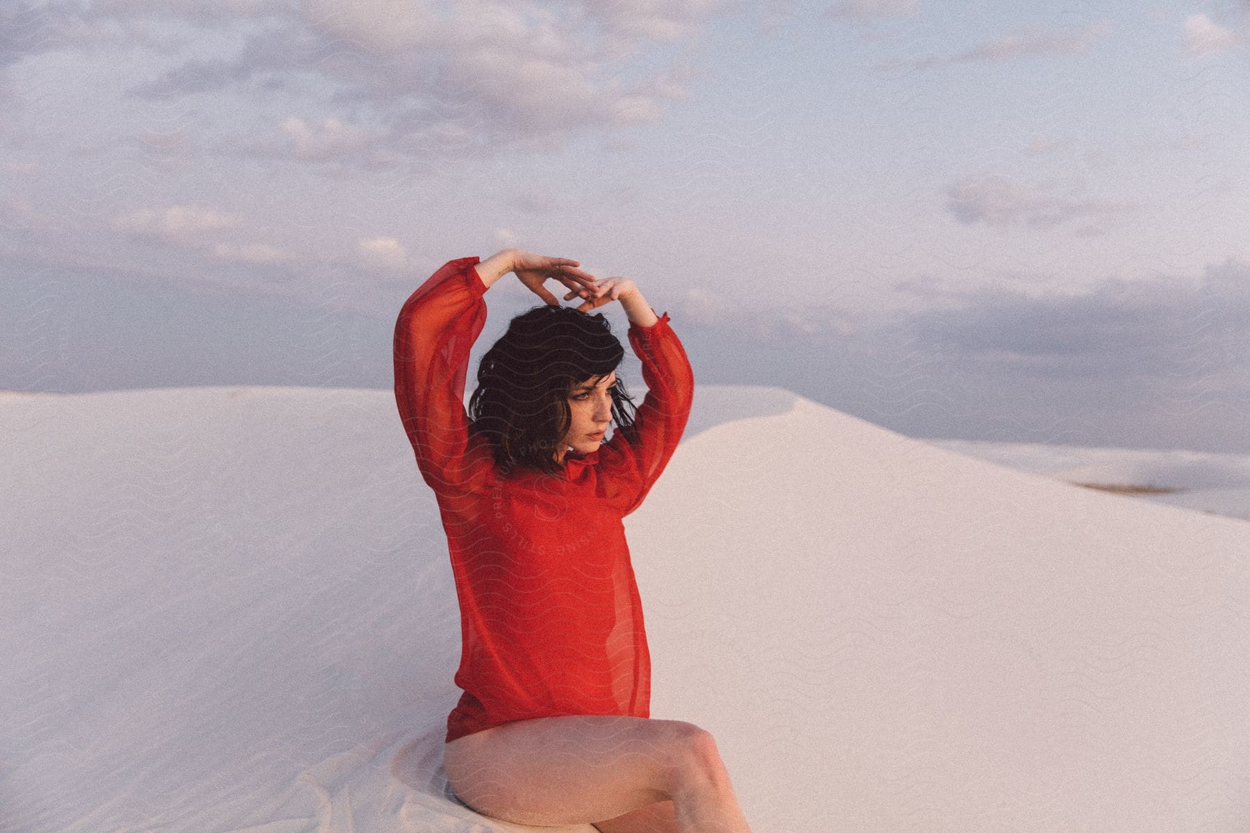 A darkhaired woman dressed in red sits on snow in new mexicos white sands
