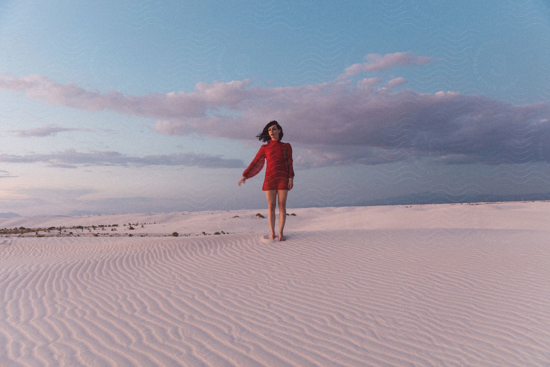 Woman In Red Dress Standing On Sand With Clouds In Background