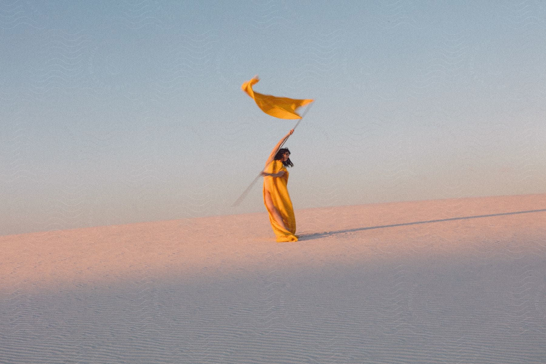 A woman in a yellow dress waving a yellow flag in the desert on a sunny day