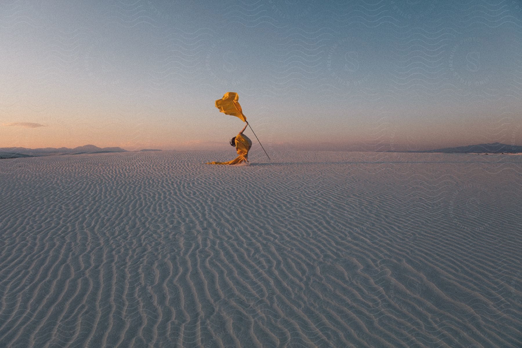 A yellowdressed dancer holds a flag in the desert twilight