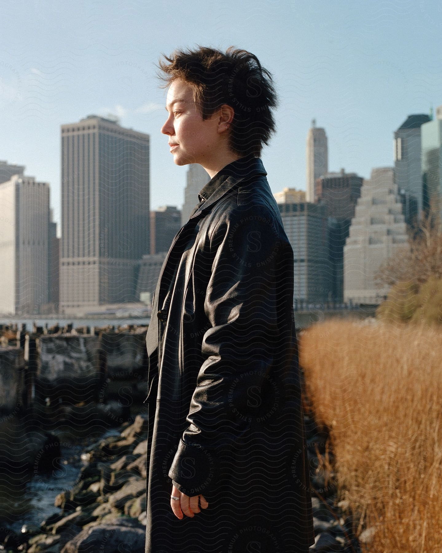 Woman with short hair and long black overcoat standing against city skyscrapers