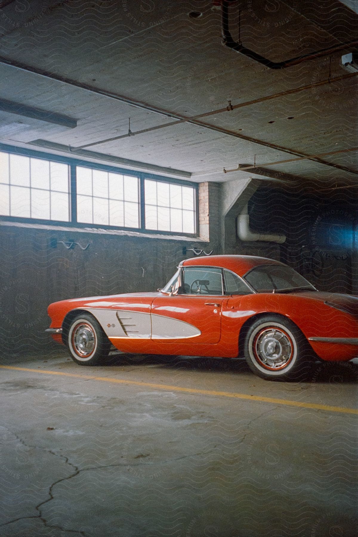 A vintage orange car parked in a garage beneath a window