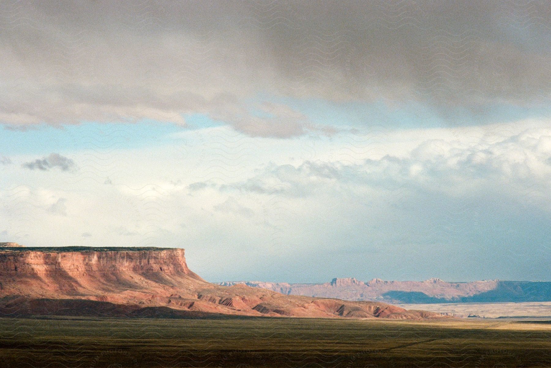 Storm clouds forming over red rock cliff plateaus and dry land fields in south west usa