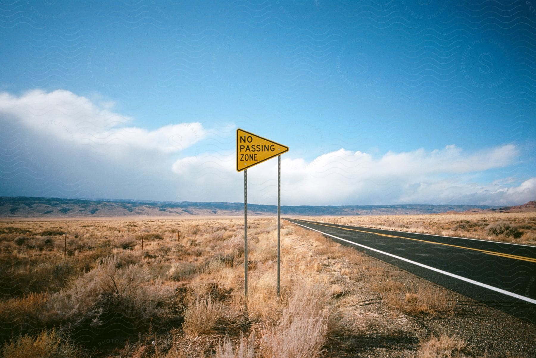 A no passing zone sign stands next to a desert highway