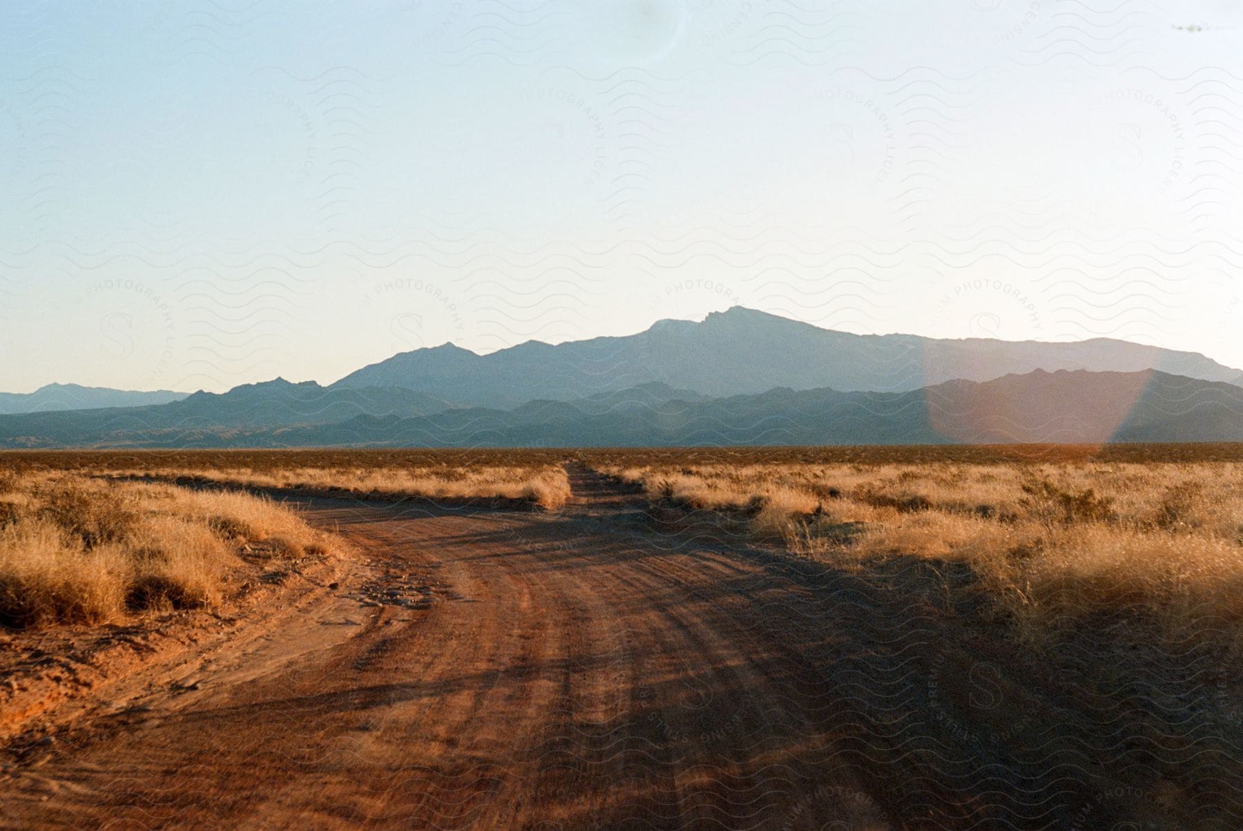 A road through the desert with dry grass and hills in the background on a sunny day