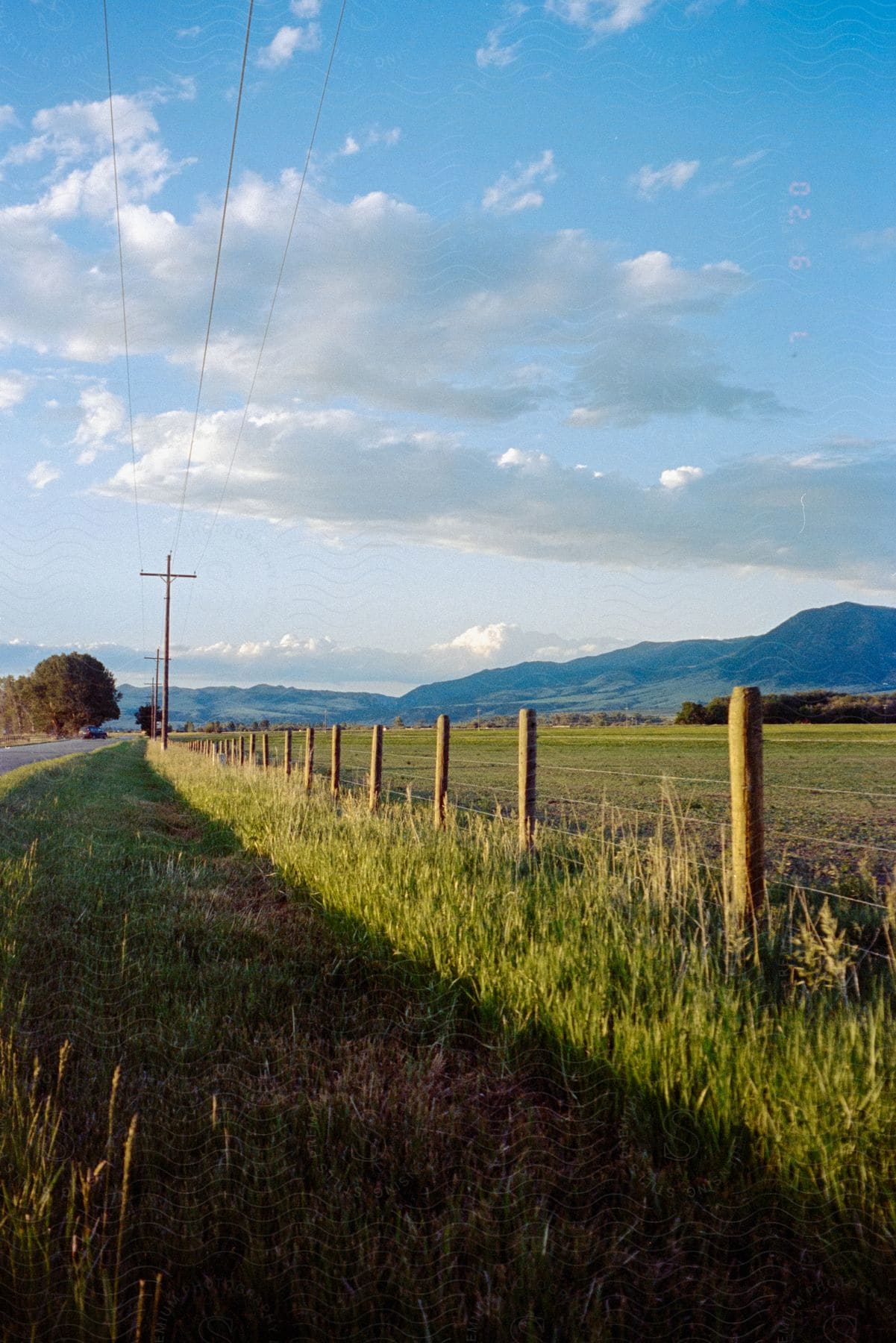 A serene countryside with mountains in the background green grassland and a fence