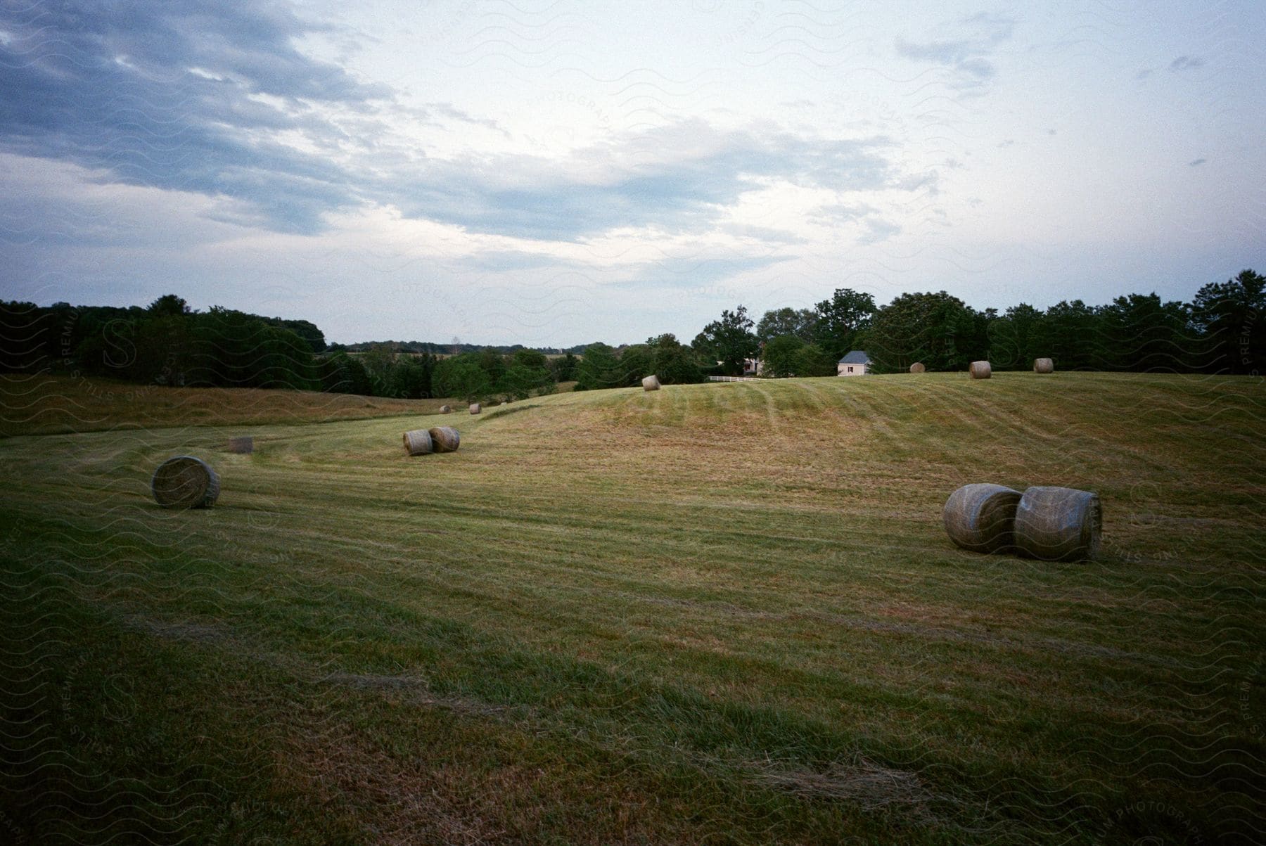 A farm house can be seen beyond hay bales in a field